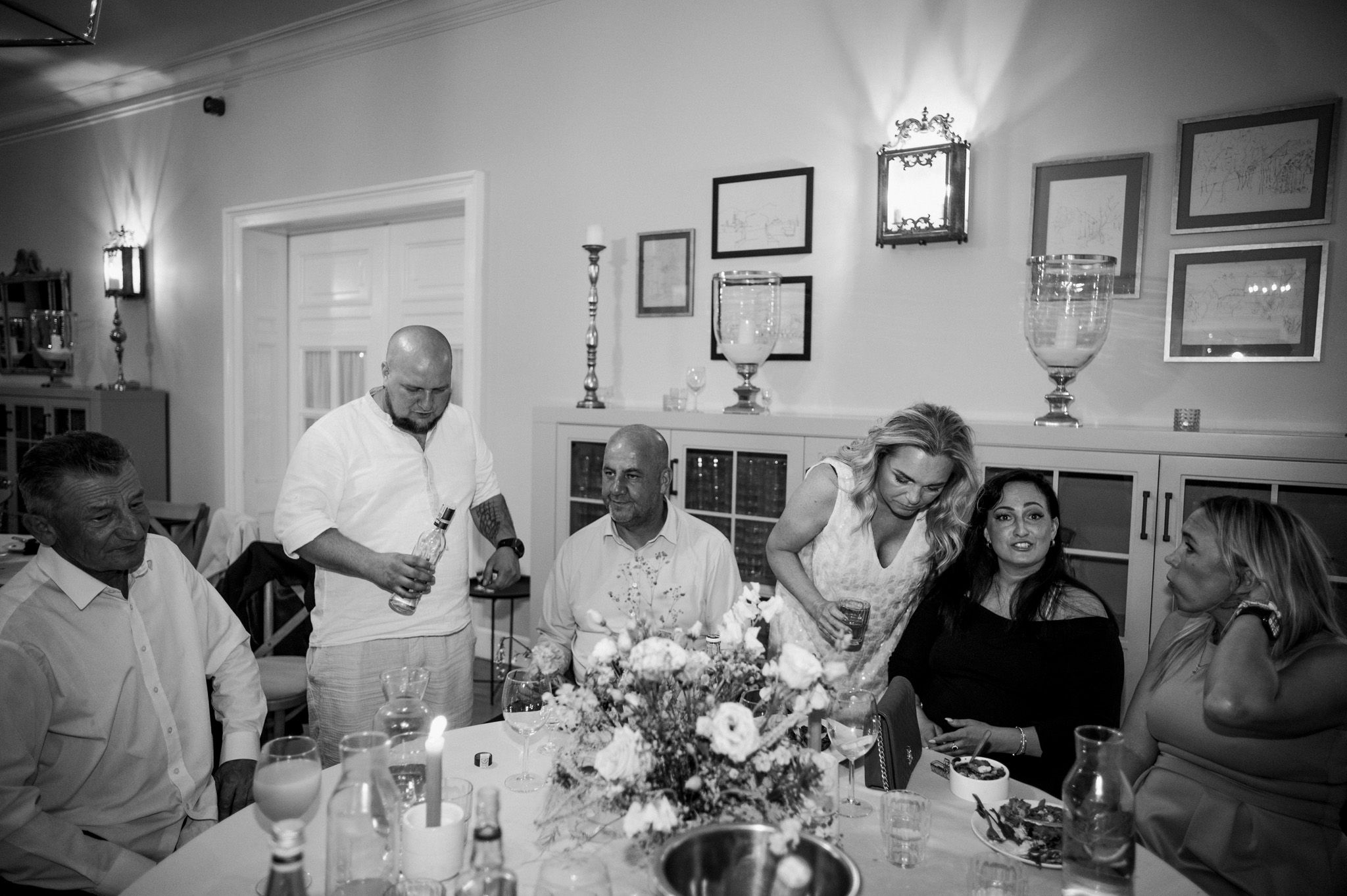Black and white photo of wedding reception dinner with guests seated at decorated table.