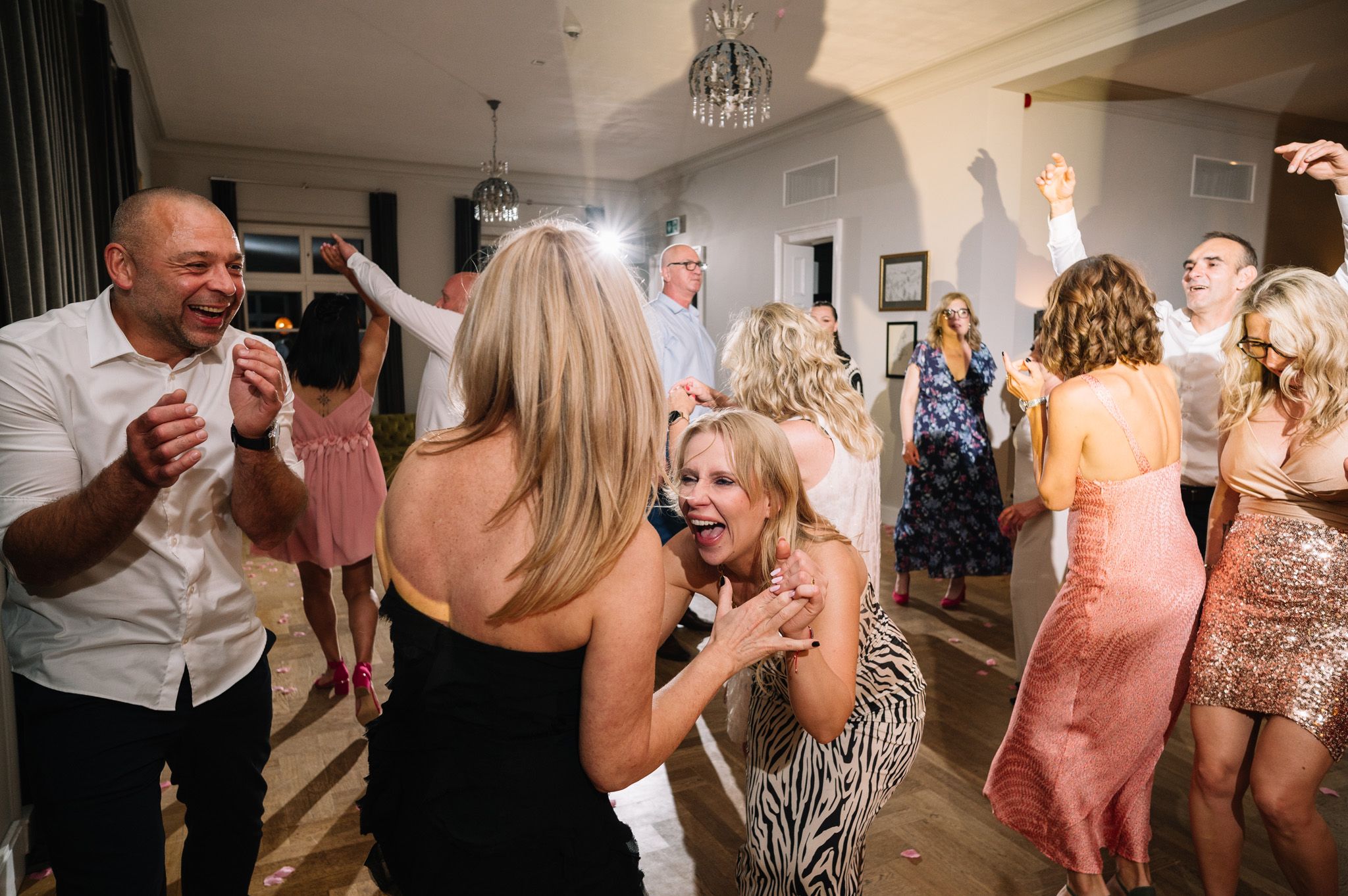 Wedding guests dance and celebrate energetically on a lively dance floor during an indoor reception.