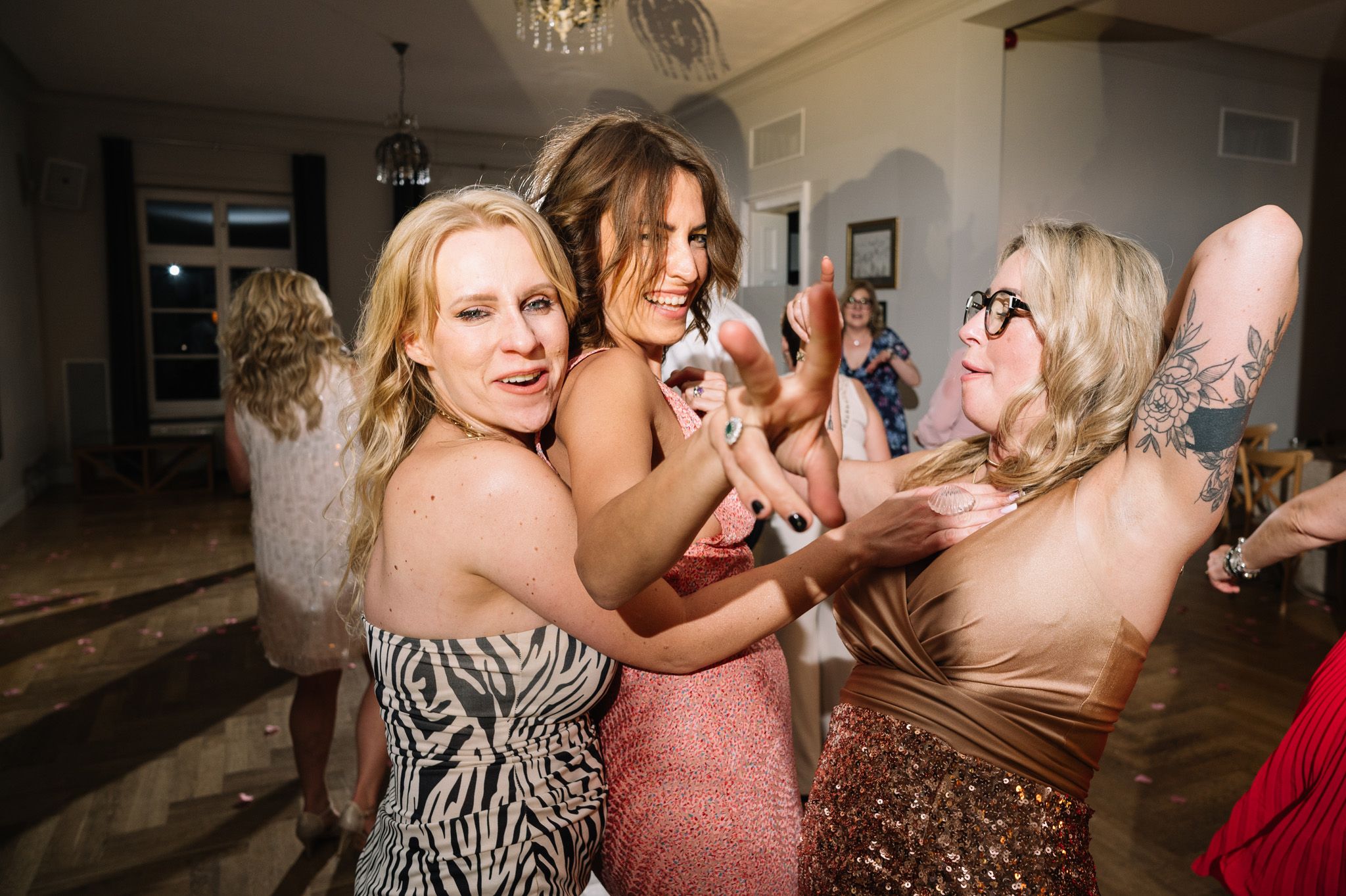 Friends in formal attire laugh and dance together at a celebration party.