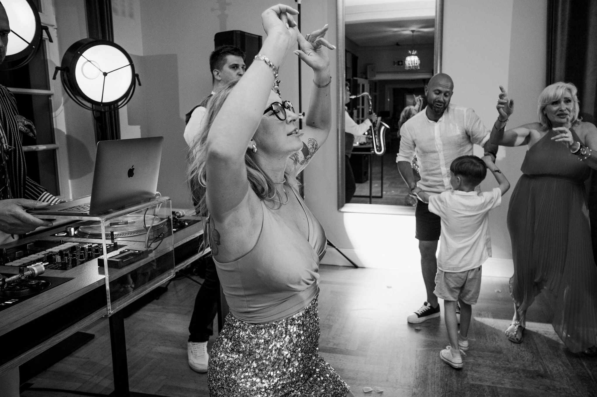 Black and white image of people dancing with DJ equipment visible in the background.