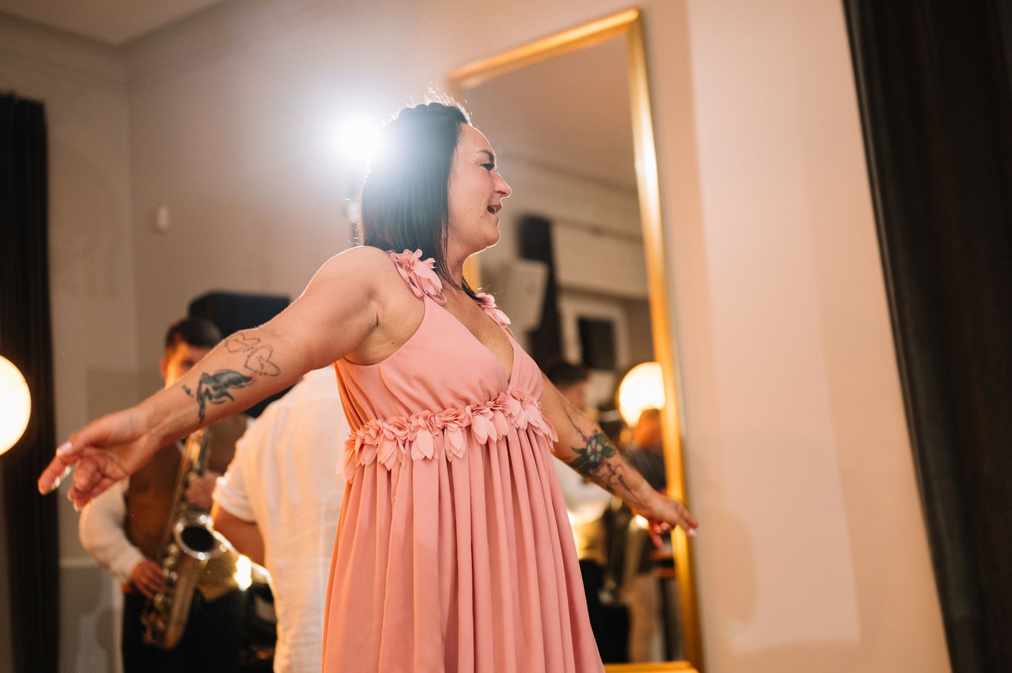 A dancer in a flowing peach dress spins joyfully on a dance floor with others visible in the background.
