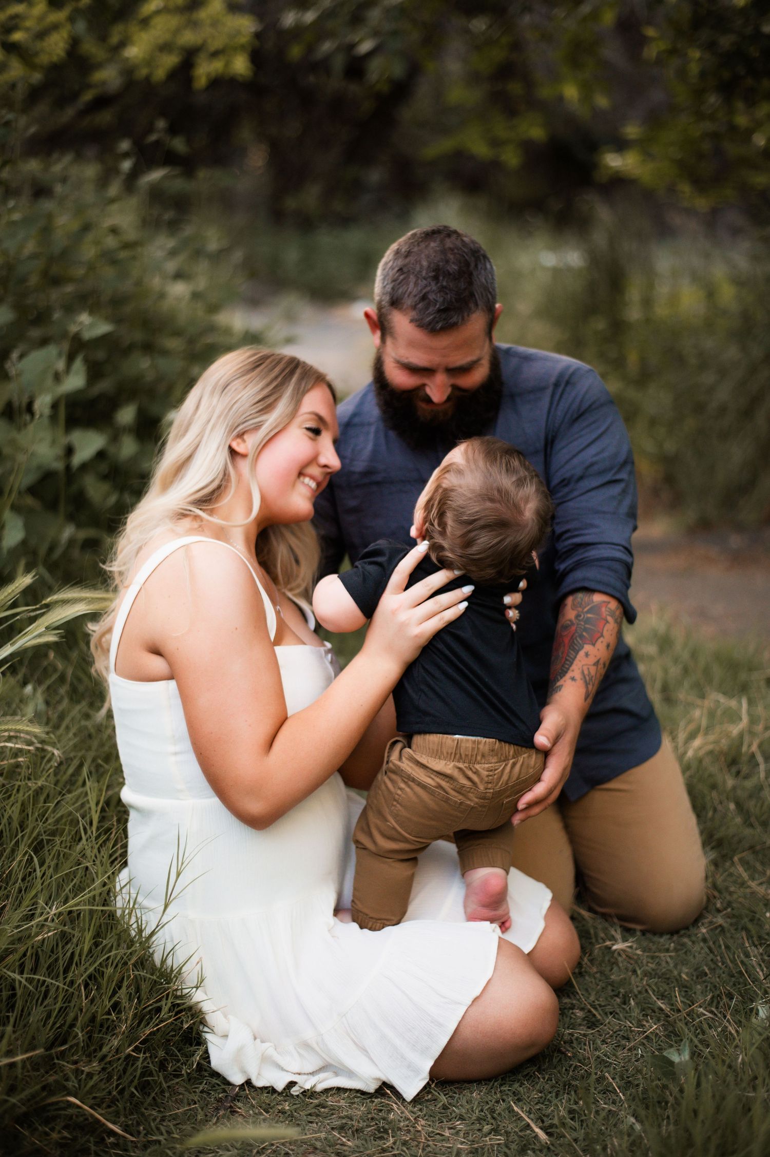 A family shares a tender moment together while sitting in tall grass during an outdoor photo session.