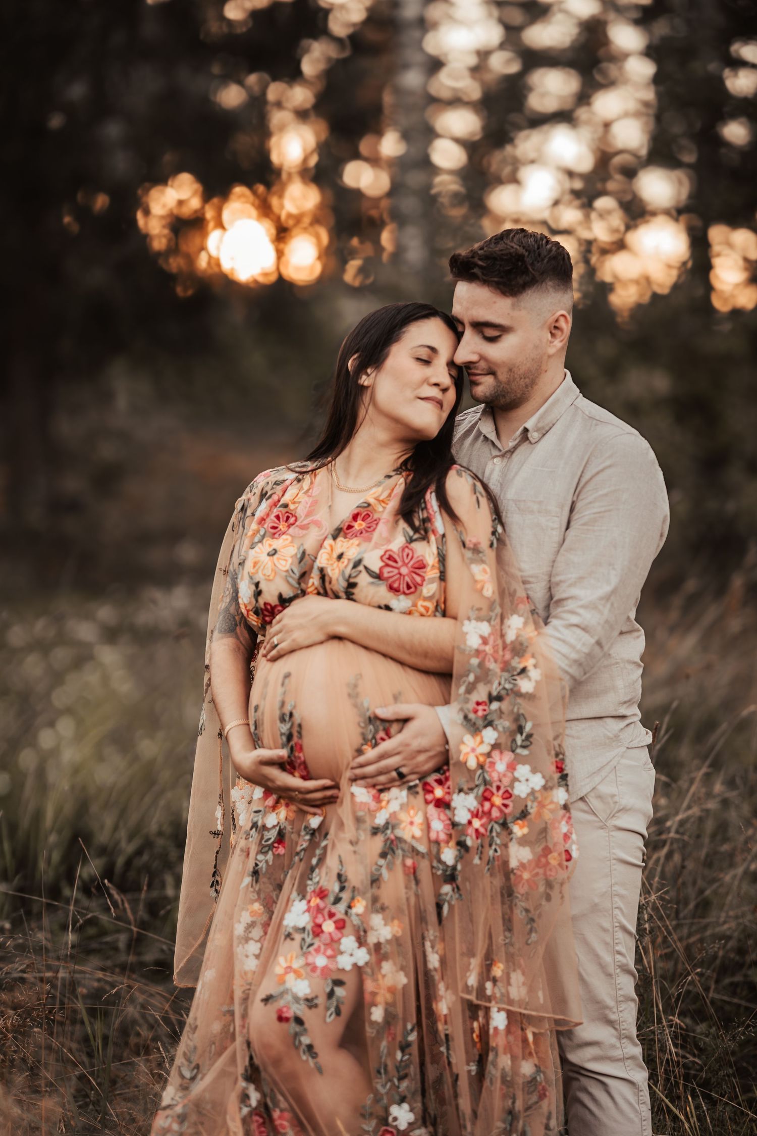 Maternity portrait featuring a floral dress and tender embrace in warm studio lighting.