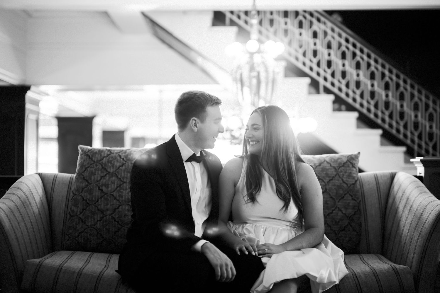 A romantic black and white photo of a couple sharing a joyful moment while sitting together on an elegant sofa.