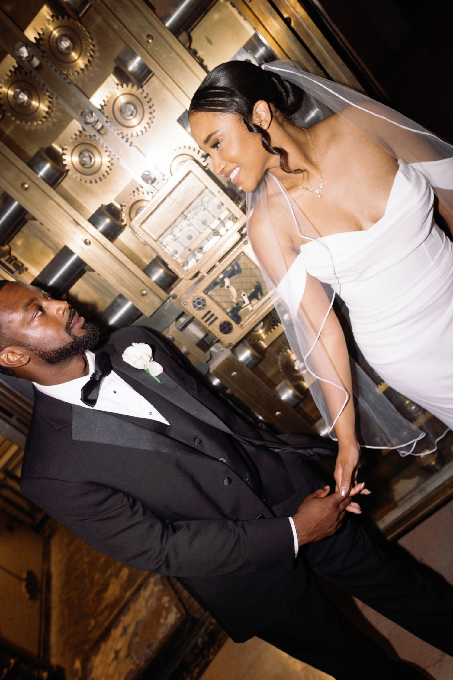 A bride and groom share an intimate moment in an ornate venue with vintage lighting fixtures.