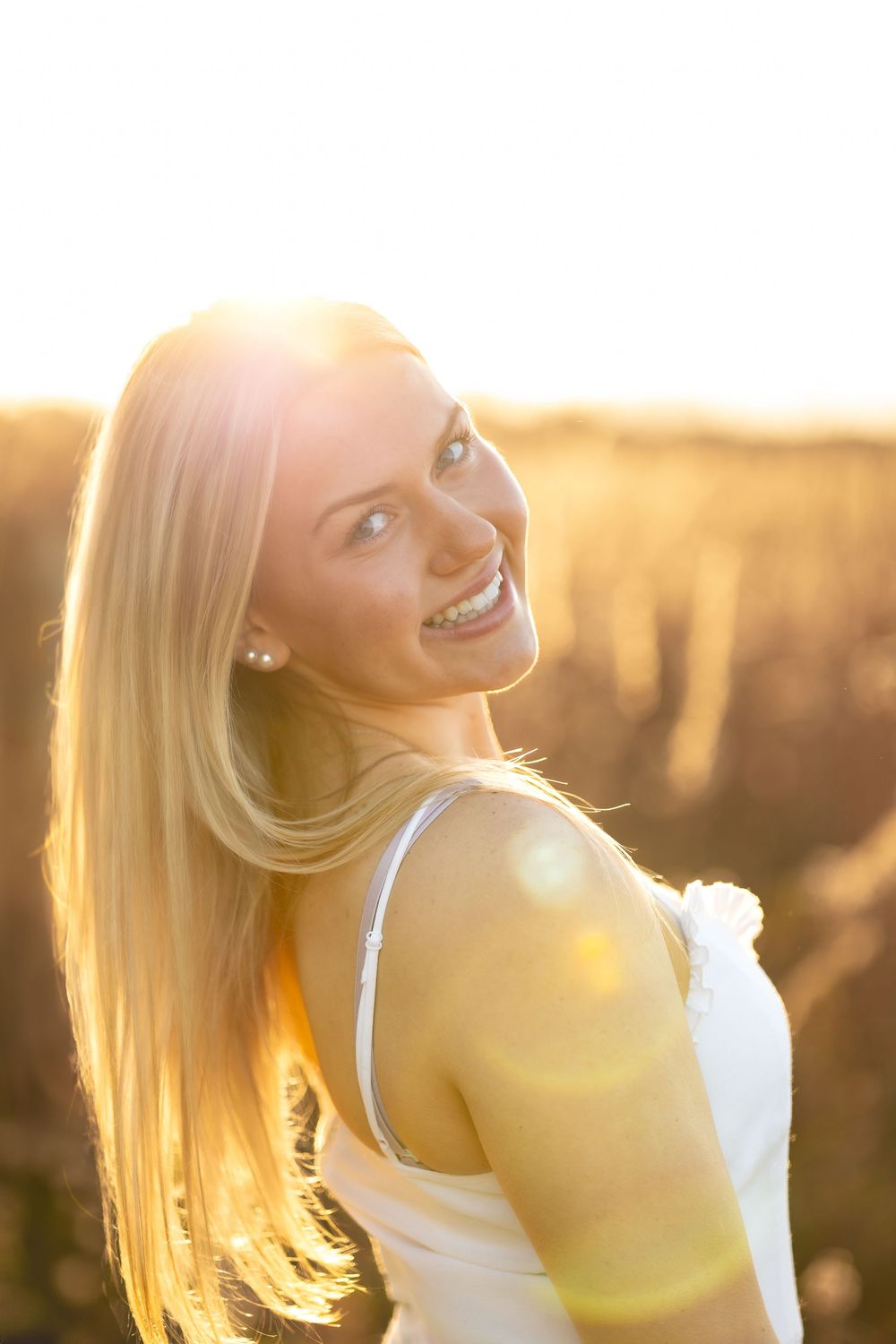 Backlit portrait of someone with long blonde hair smiling over their shoulder during golden hour sunset.
