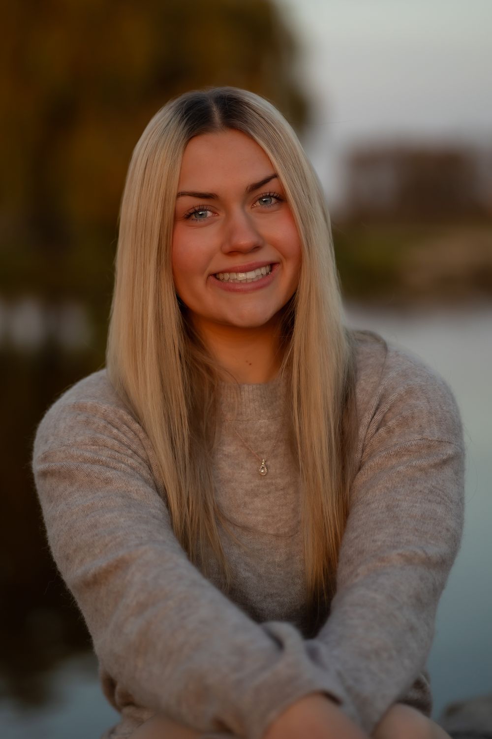 Close-up portrait in a gray sweater with autumn scenery in background.