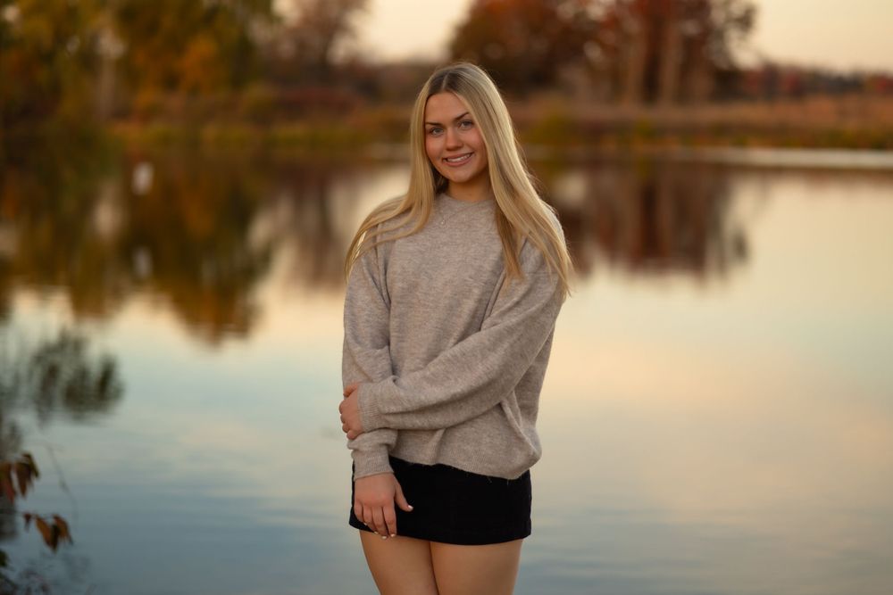 Portrait by a lake wearing a beige sweater and shorts at sunset.