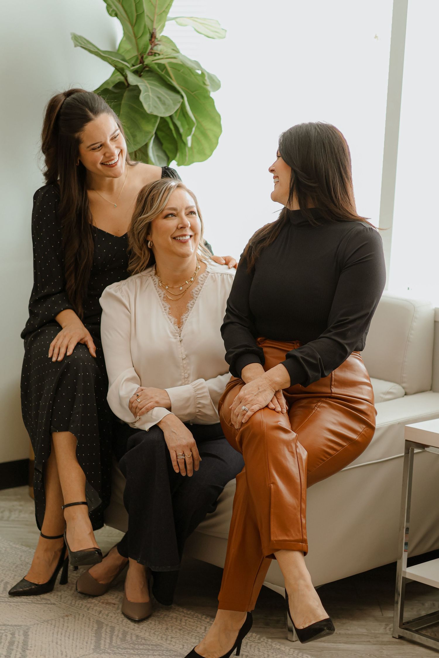 Candid photo of three women laughing together on modern gray couch.