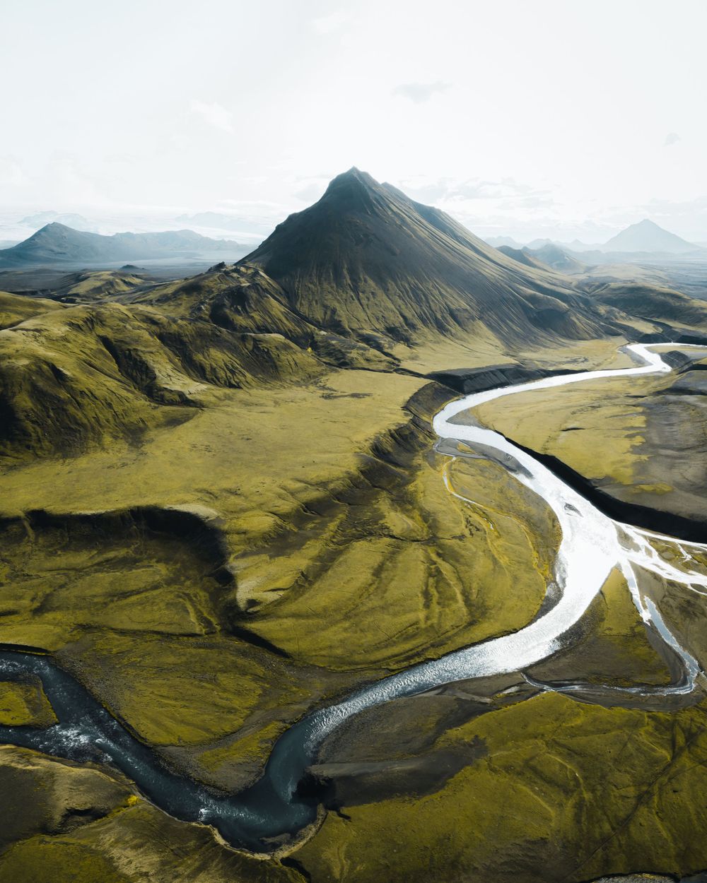Aerial view of a winding river valley with green hills and mountains in Iceland's scenic landscape.