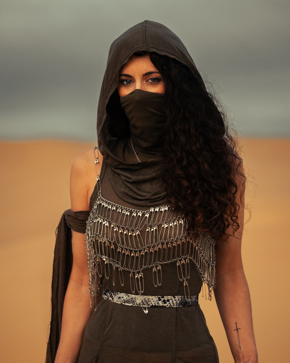 Woman wearing a black headscarf and silver statement necklace poses against a desert backdrop.