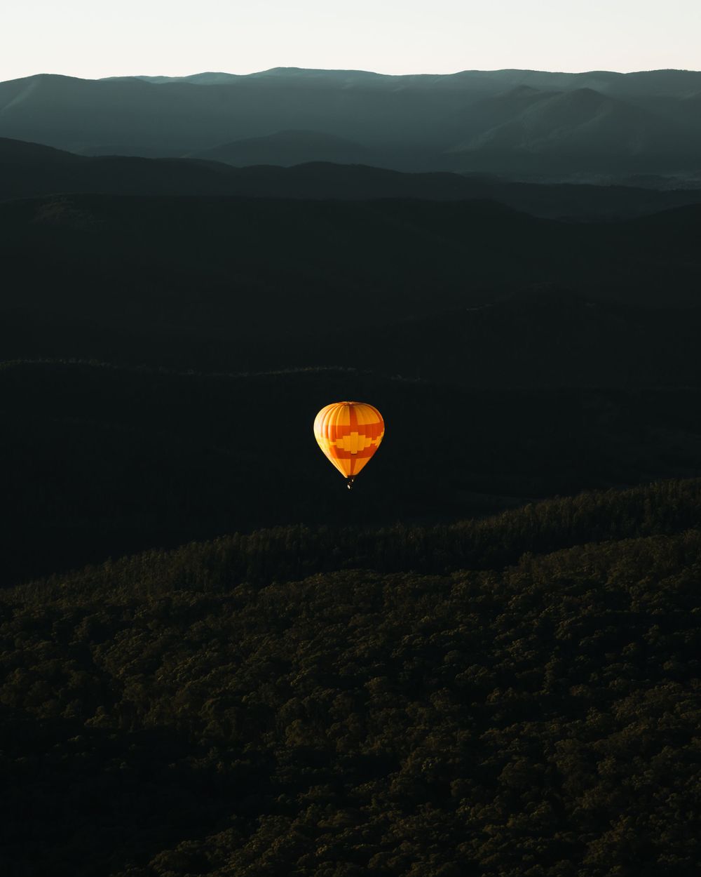 Orange hot air balloon glows against dark mountain landscape at dusk.