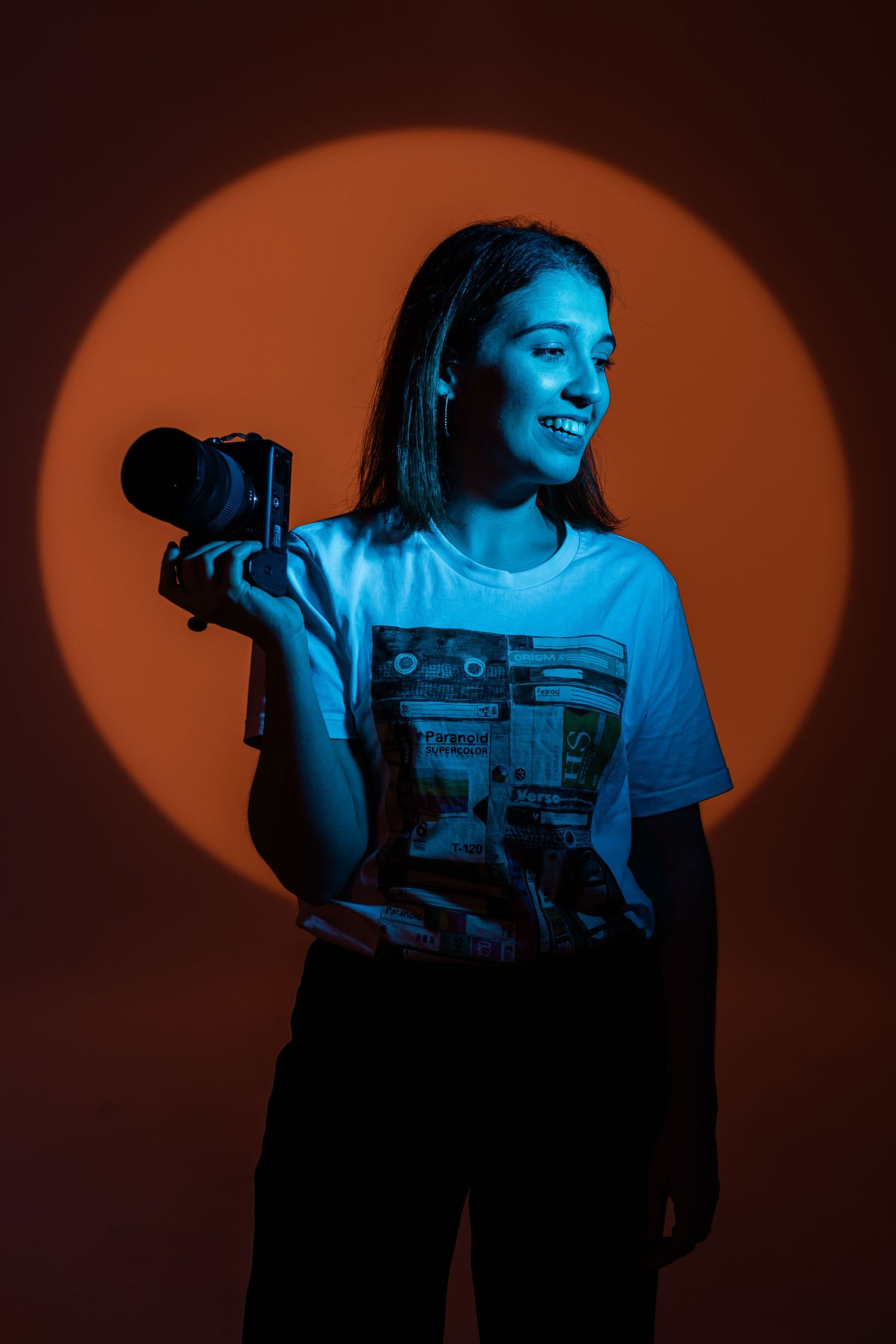 Creative portrait of photographer with camera against orange circular backdrop lighting.