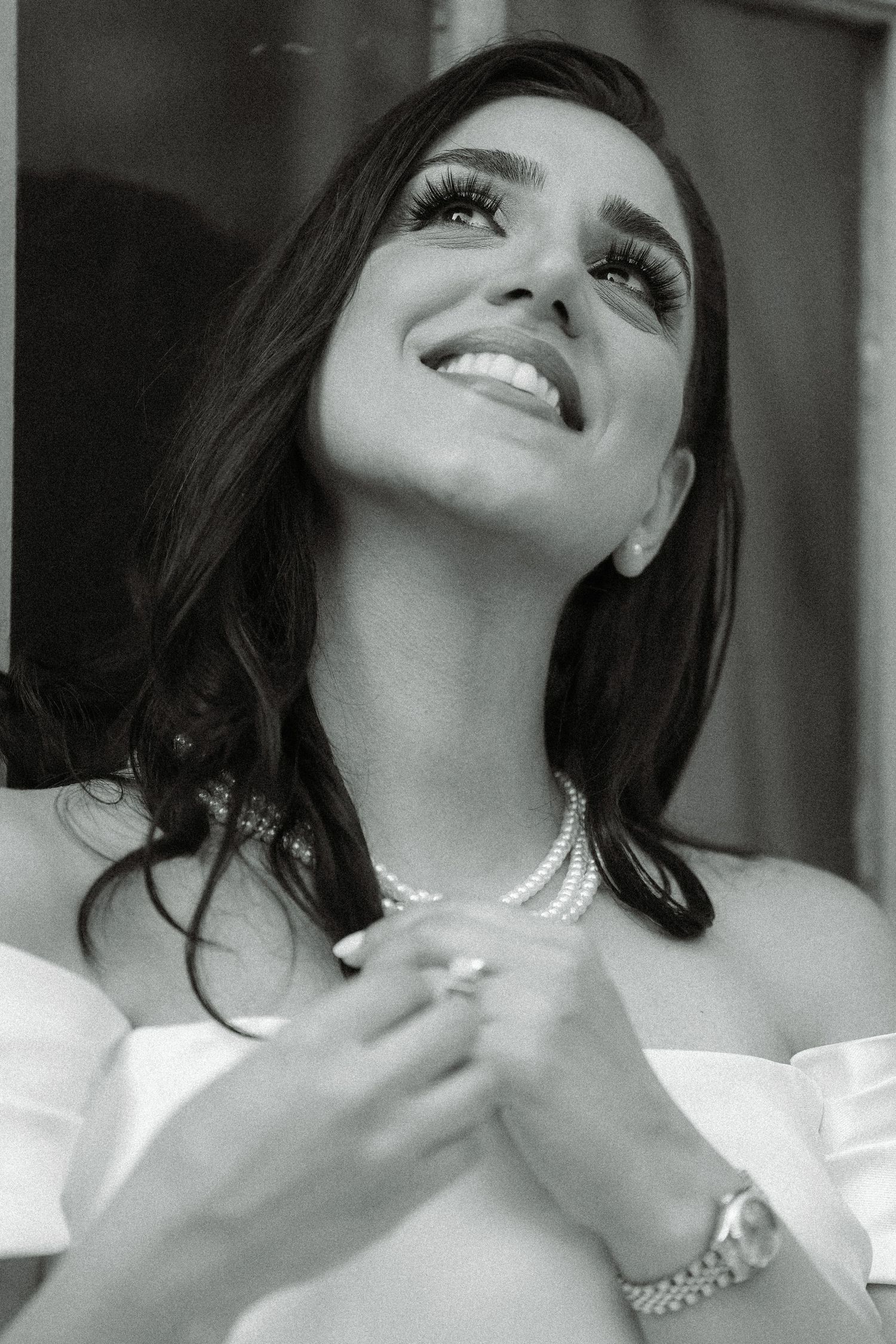 Portrait of a smiling woman in white wearing jewelry and an off-shoulder dress.