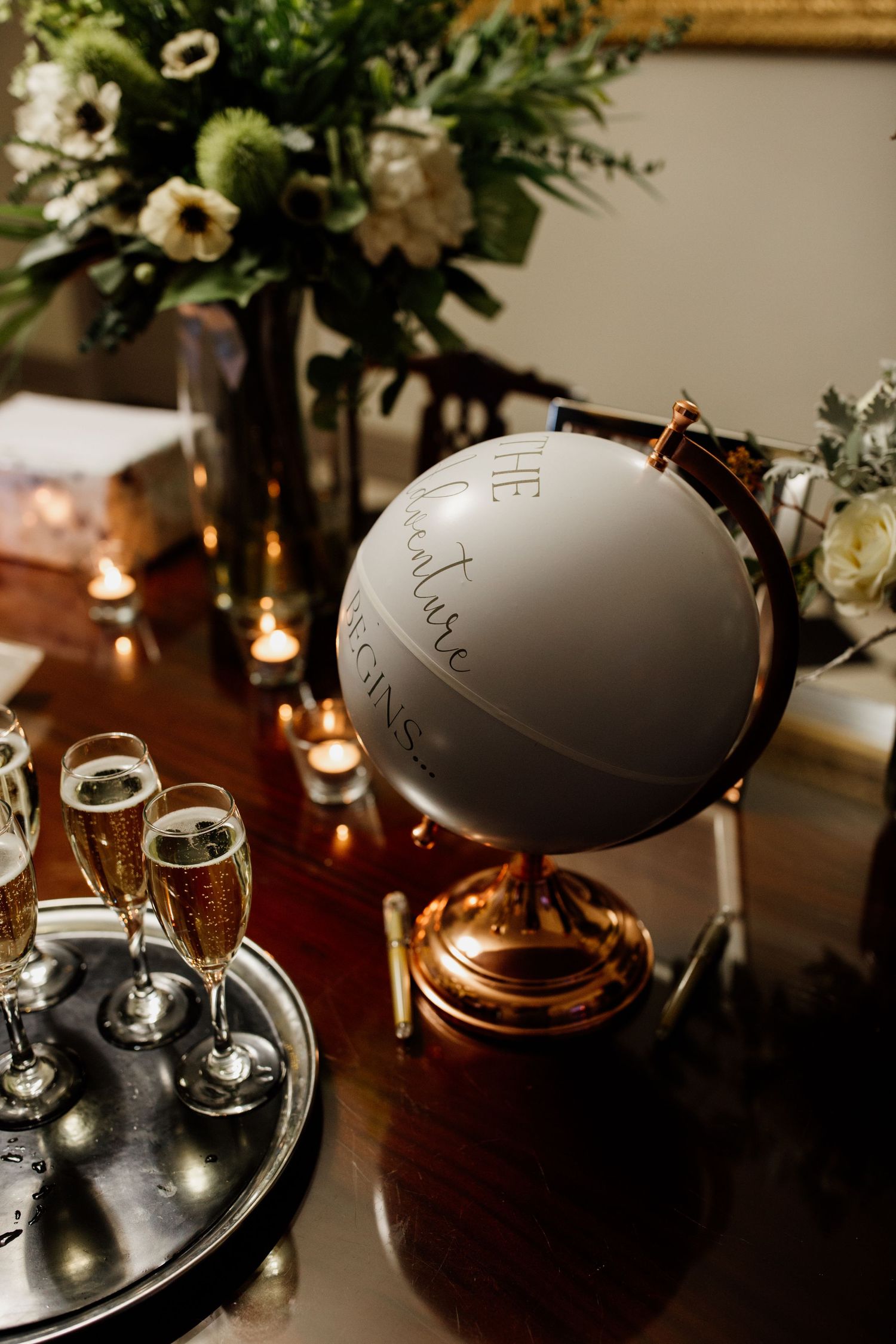 Elegant table setting with decorative gray globe, champagne glasses, and floral arrangements in moody lighting.