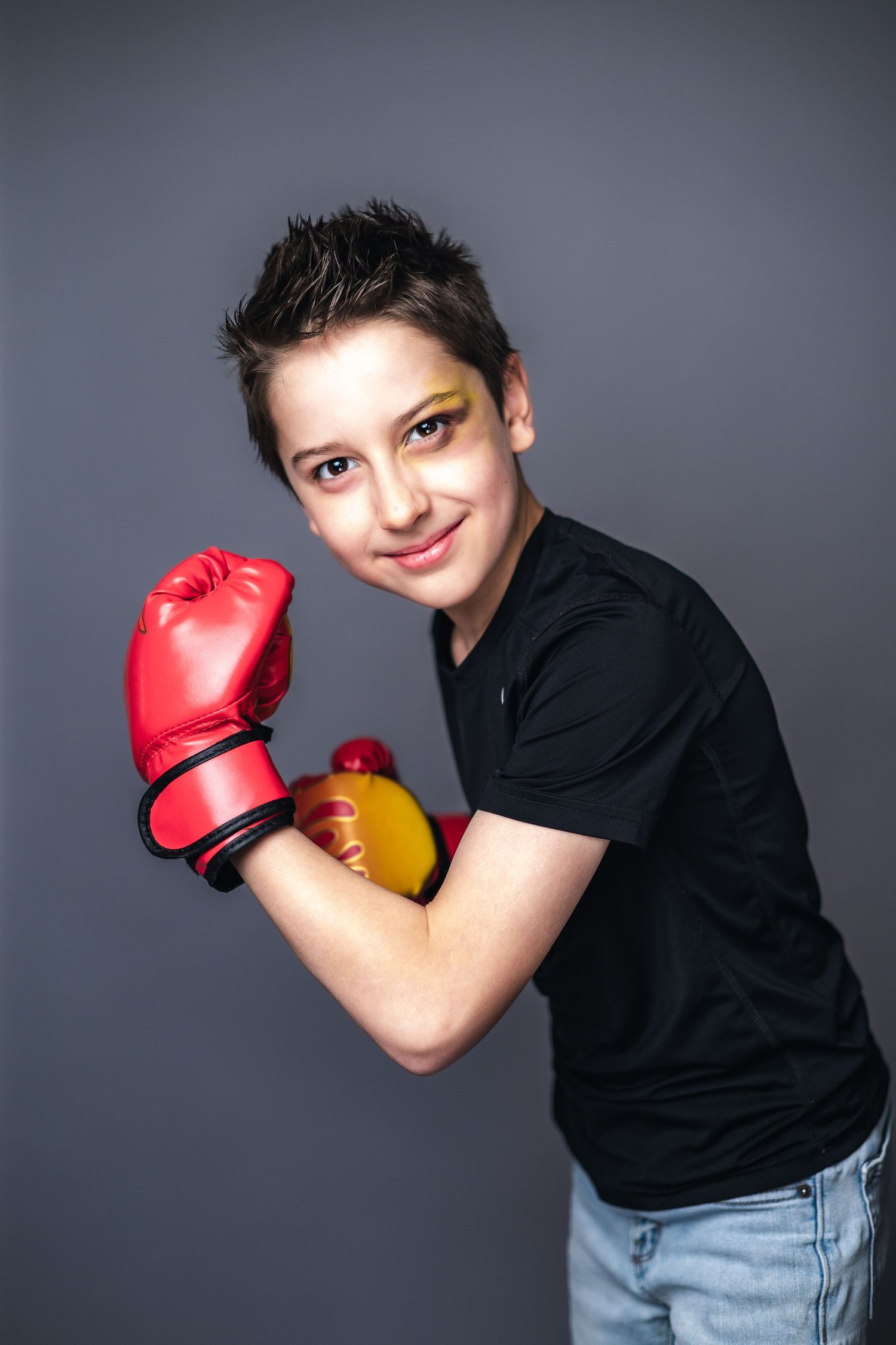 Athletic person wearing a black t-shirt strikes a boxing pose with red gloves against a gray background.