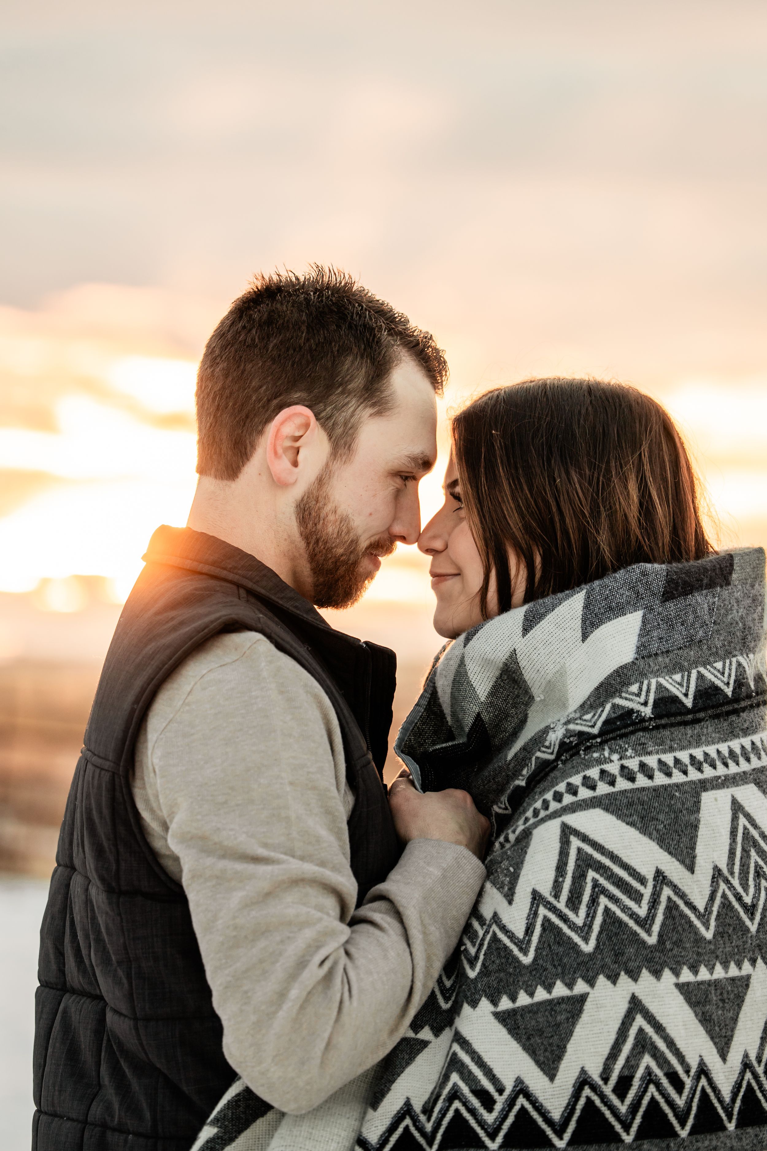 guy wrapping his girl with a blanket with sunset behind