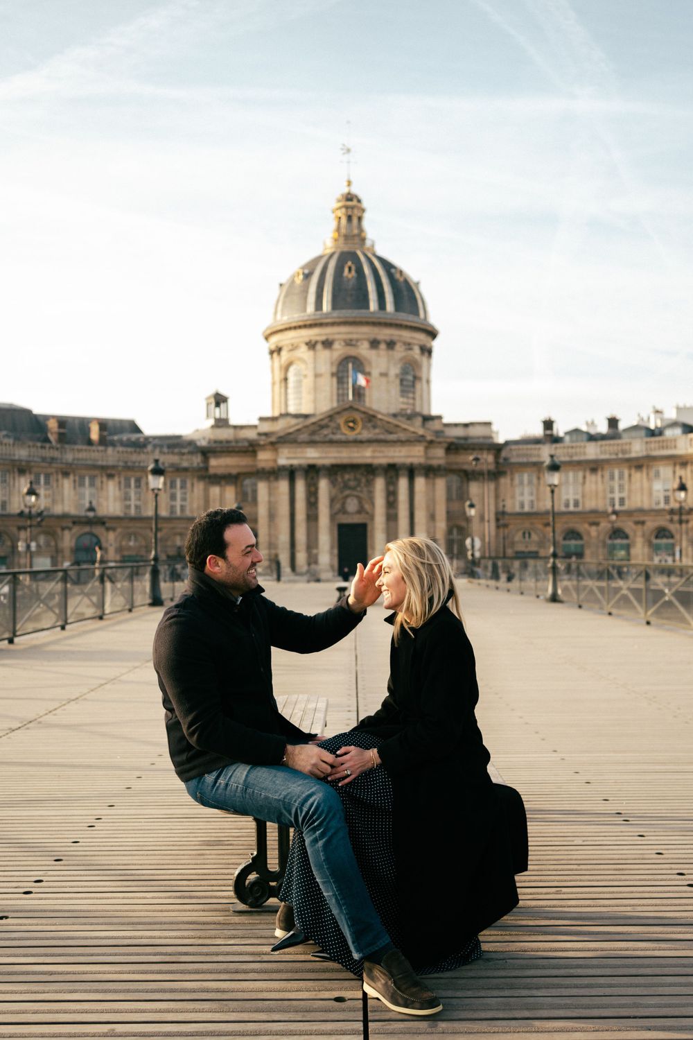 A couple shares an intimate moment on the Pont des Arts bridge with Institut de France dome in Paris.