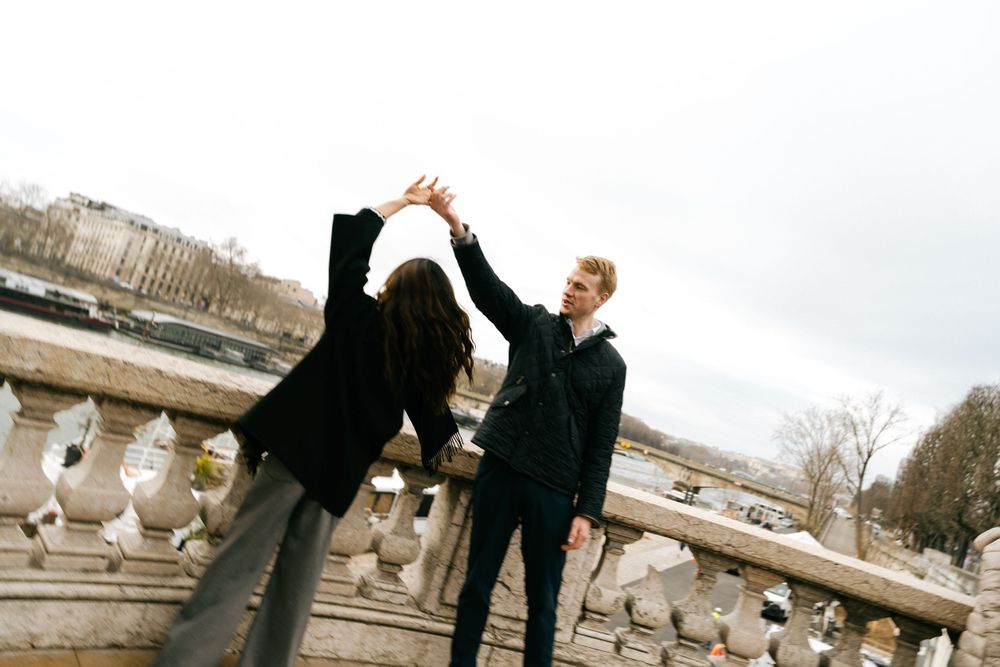 Two stylishly dressed people dancing on stone steps outdoors with a cloudy sky in the background.
