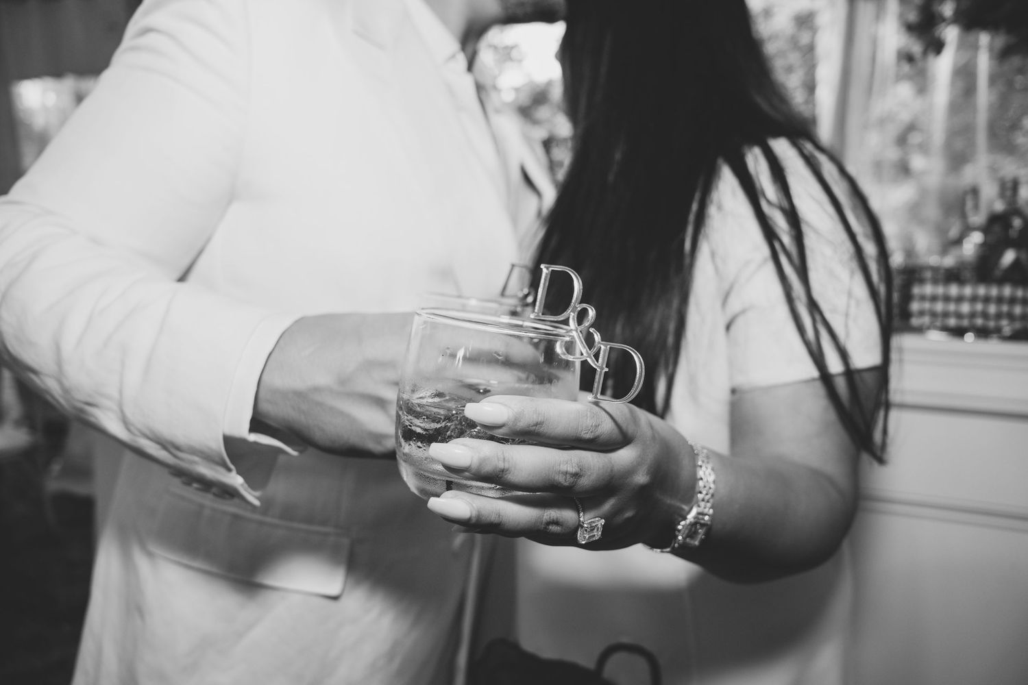 Close-up black and white shot of hands holding glasses of drinks at a social gathering.