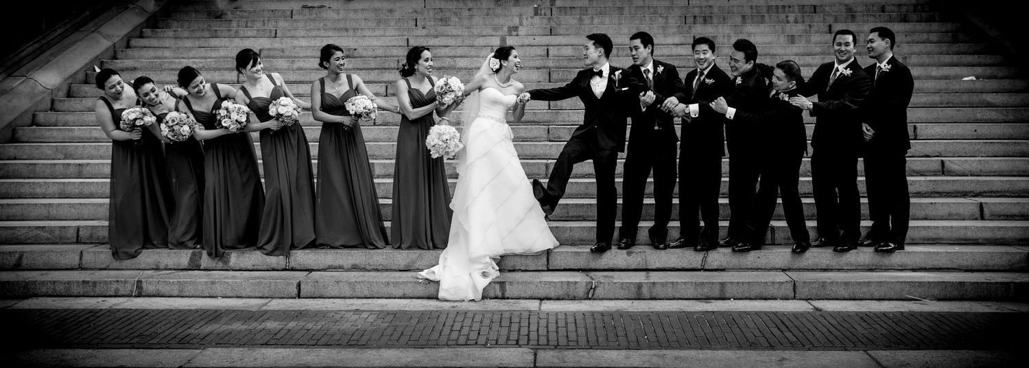 Black and white photo of wedding party standing on stone steps in a dramatic side angle composition.