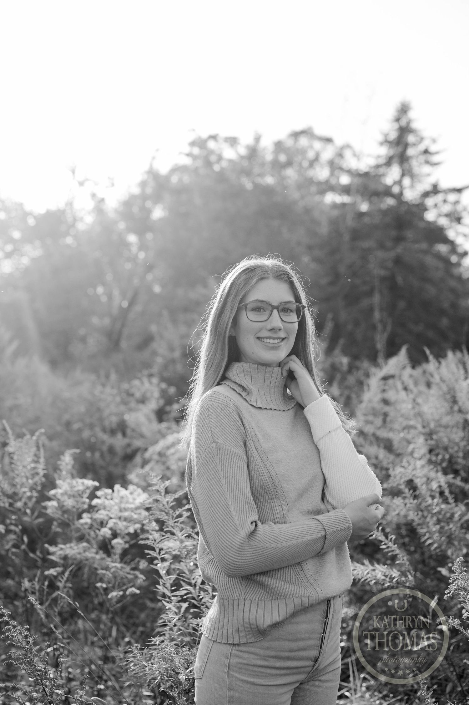 A black and white portrait taken outdoors among natural foliage and filtered sunlight.