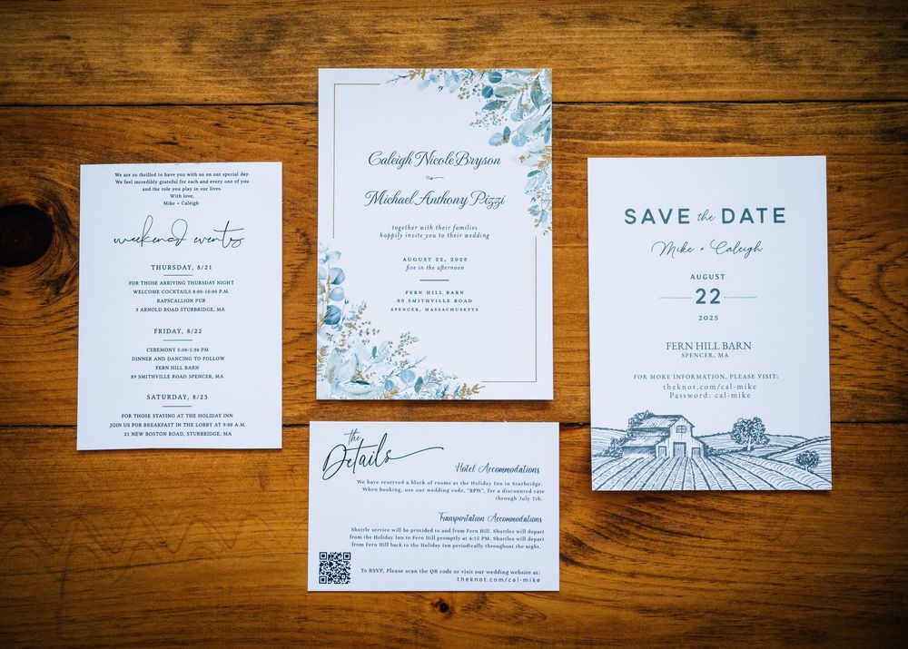 Wedding invitation suite with blue floral details and save the date cards displayed on rustic wooden surface.