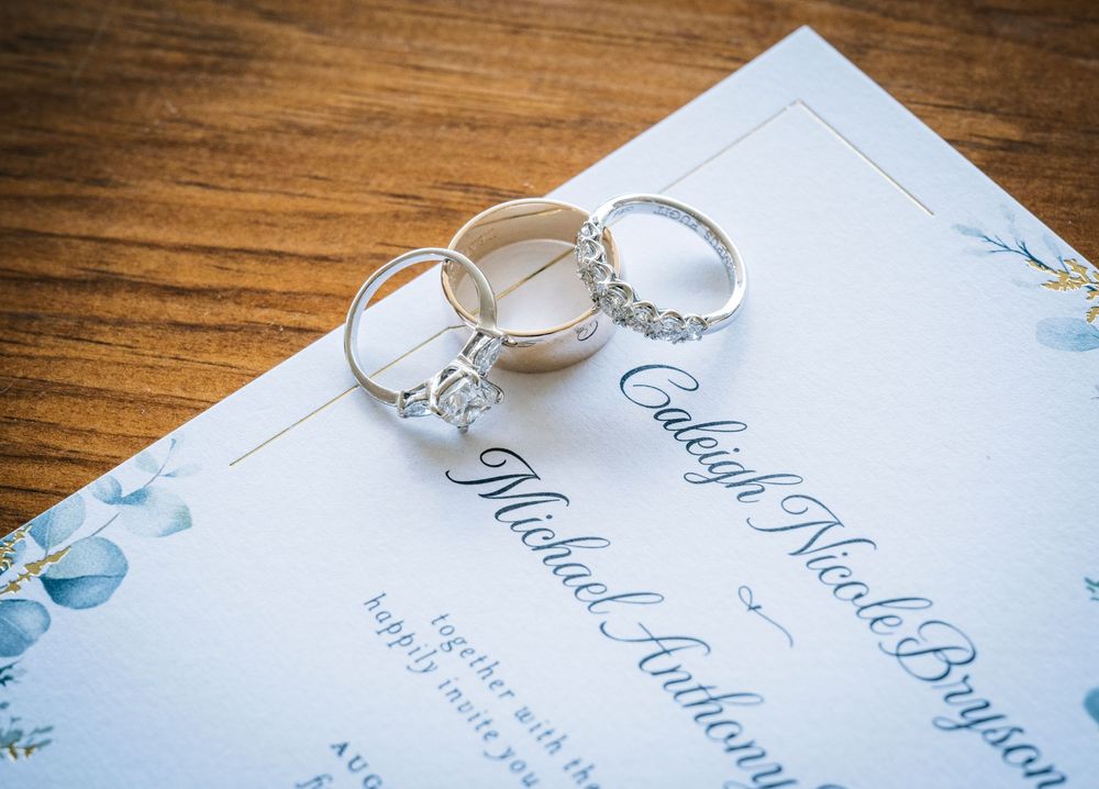 Wedding rings and elegant invitation cards displayed on a rustic wooden surface with delicate blue floral details.