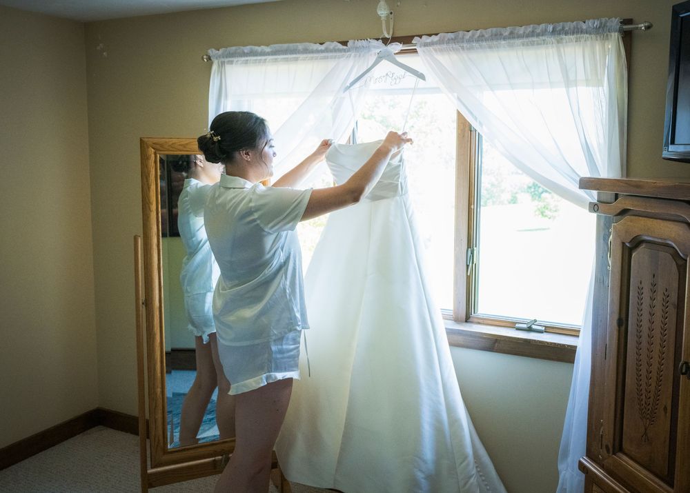 Sunlight streams through curtained windows as a white dress is prepared in a room.