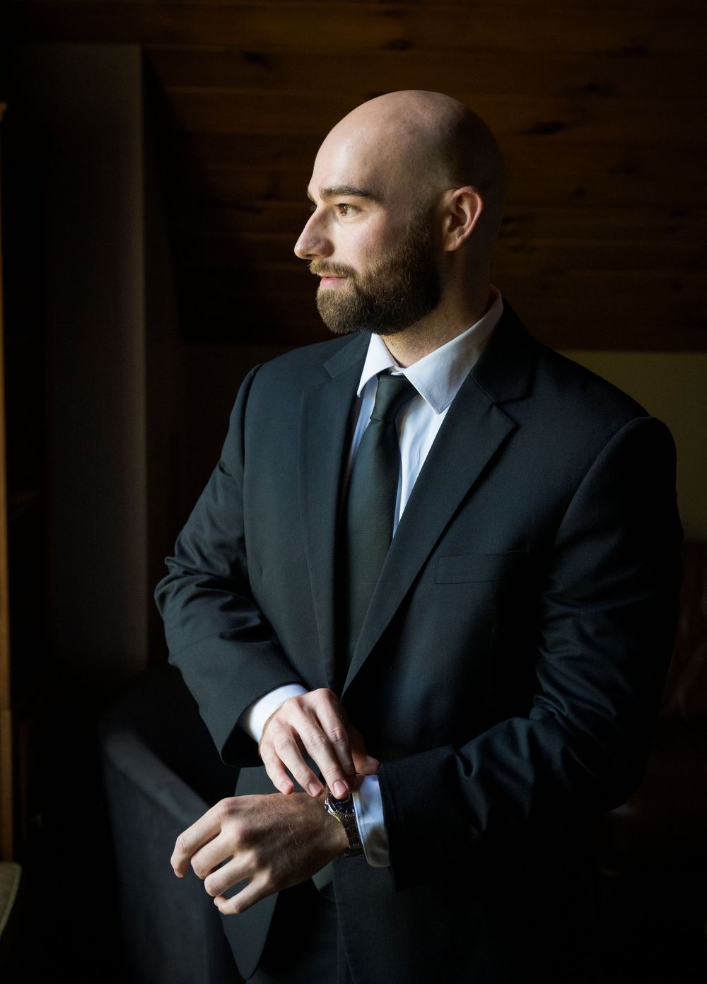 Professional business portrait of person in dark suit against dramatic lighting in moody indoor setting.
