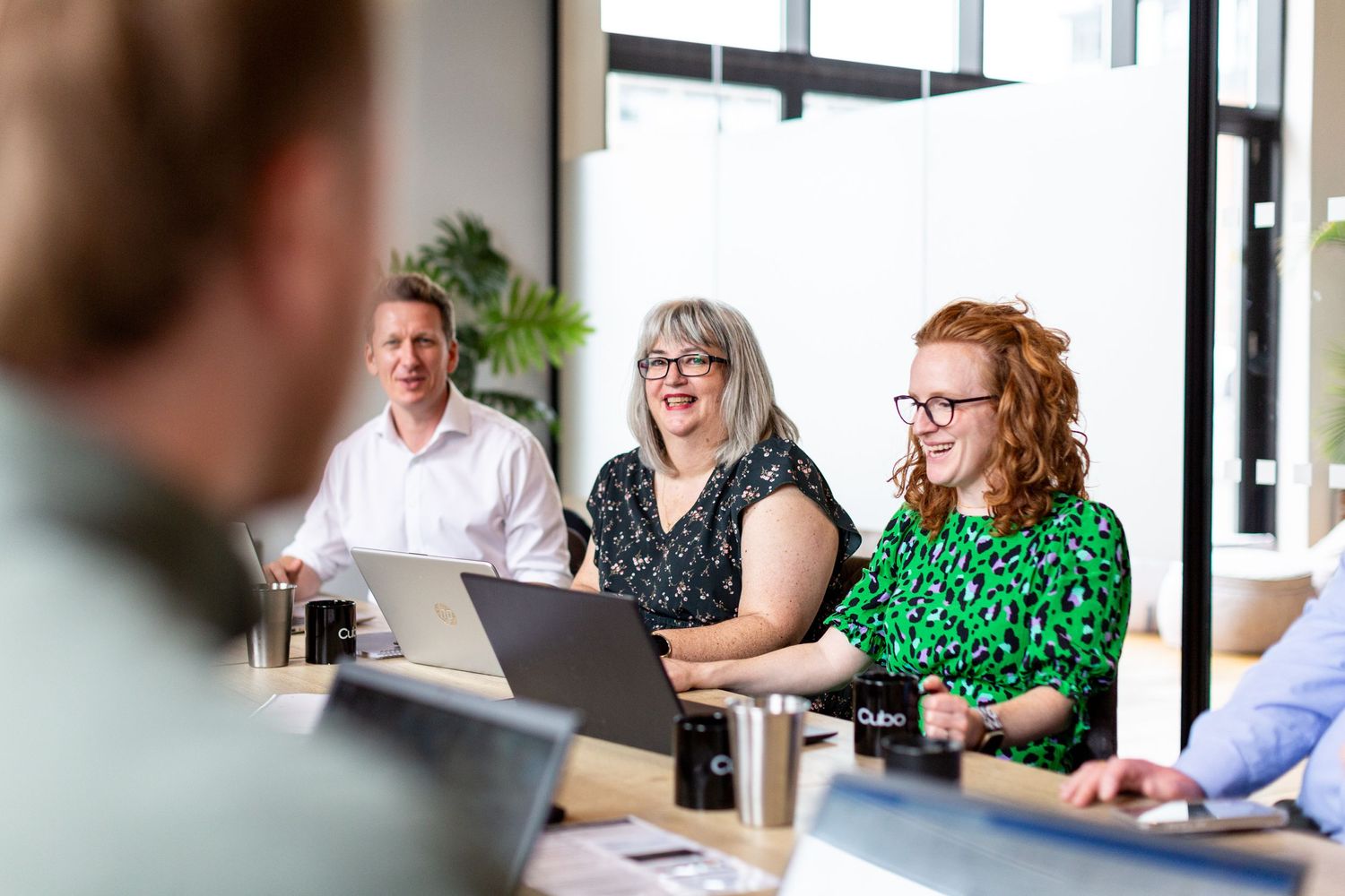 Coworkers engaged in an animated discussion during a meeting around a conference table with laptops.