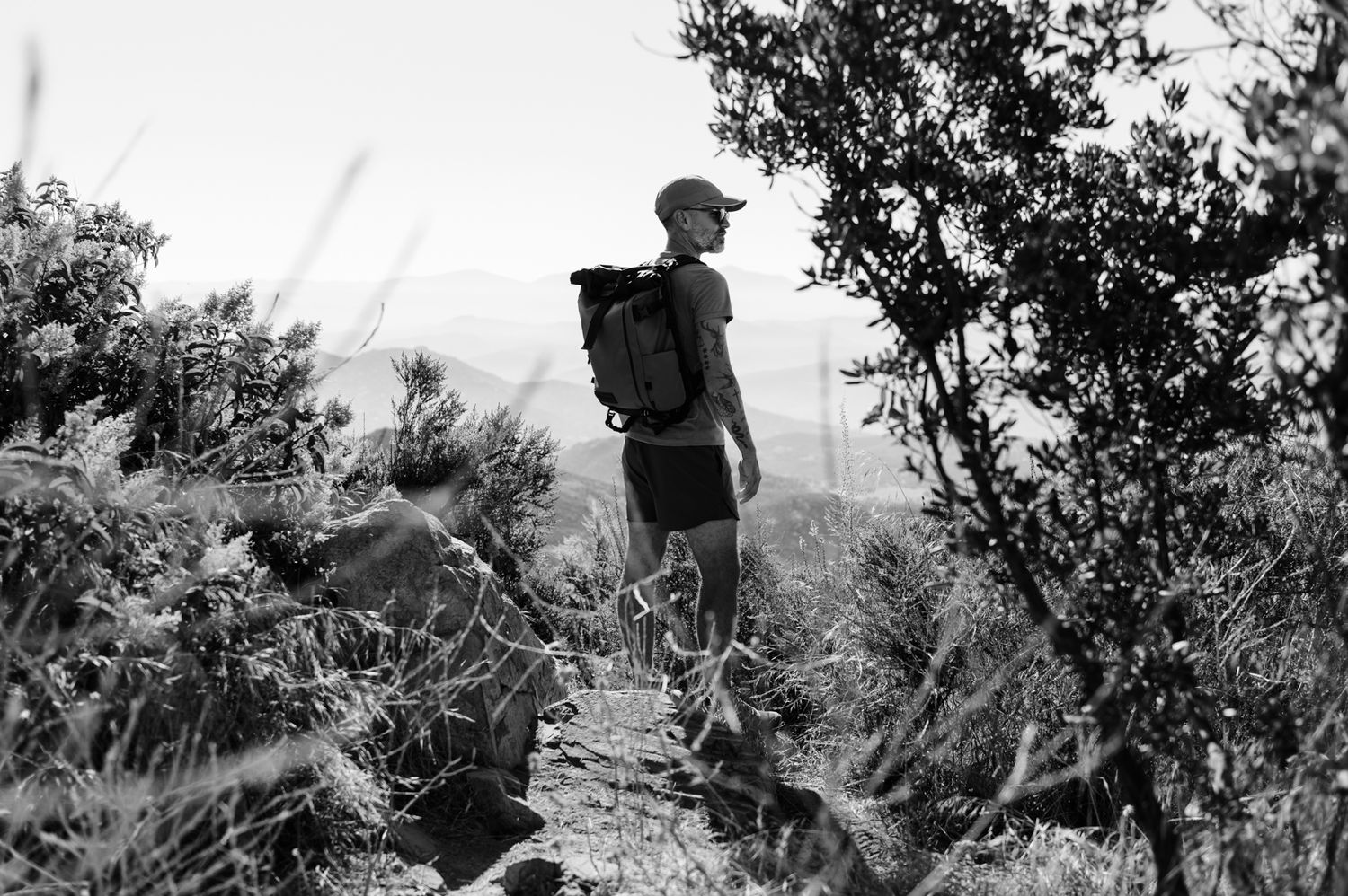Iron Mountain | Poway, CA | San Diego, California | A hiker with a backpack stands silhouetted on a mountain trail surrounded by foliage.