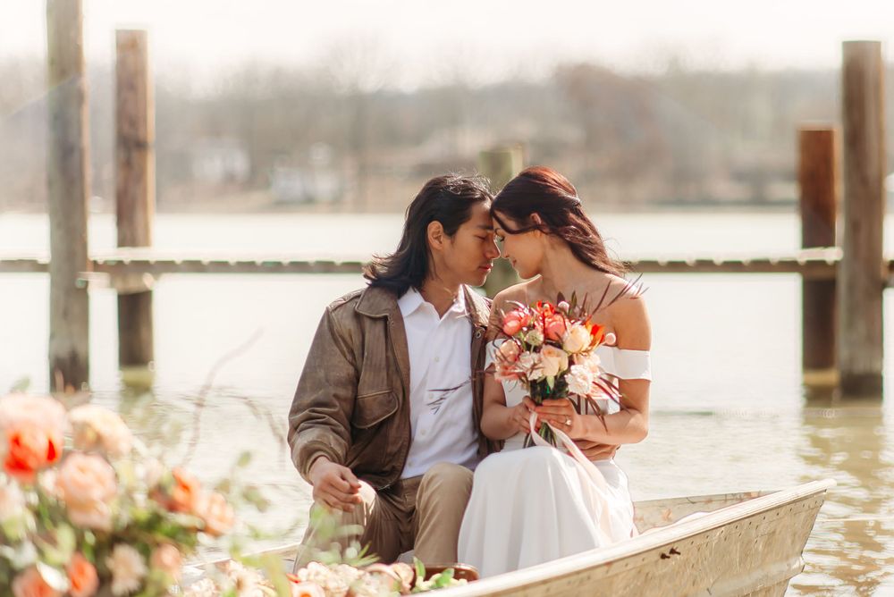 Intimate waterfront wedding photo with couple embracing and holding a vibrant bouquet.