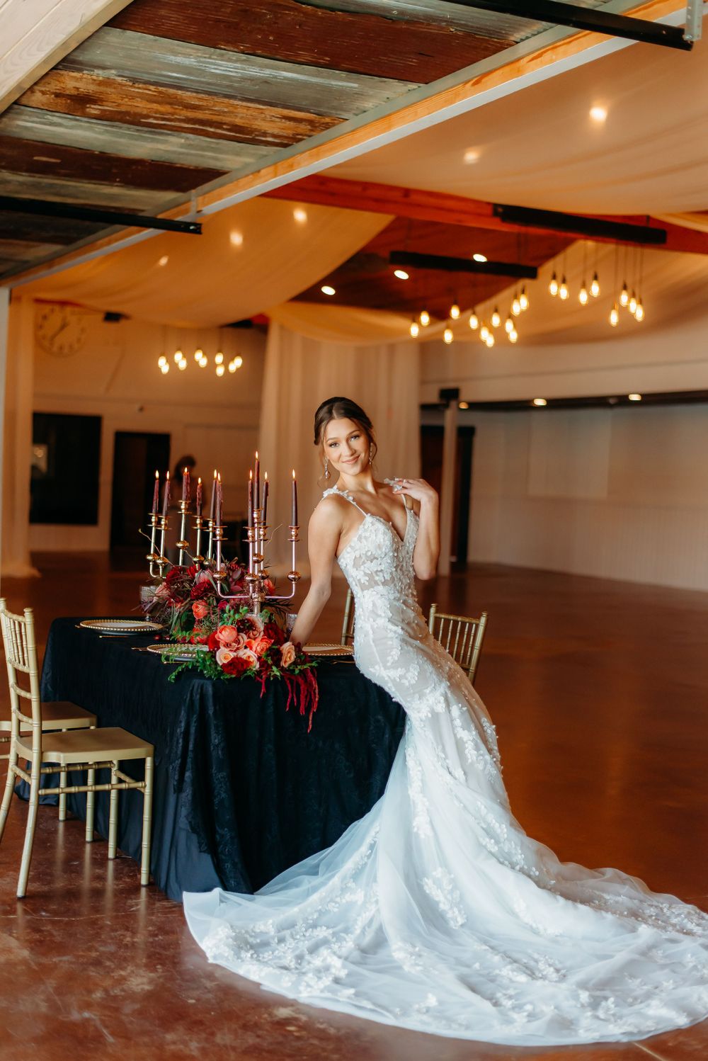 Wedding reception setup with bride in lace gown near elegant table with black linens and candelabras.