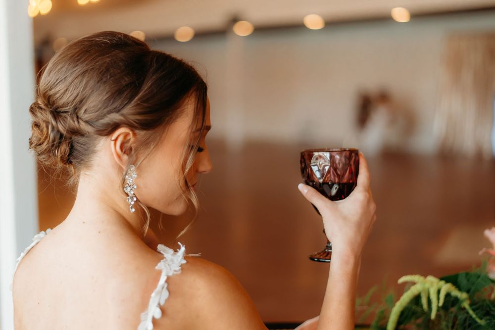 Back view of person in formal dress holding red wine glass at event.