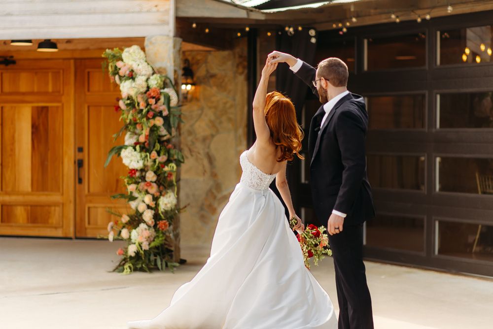 A couple shares a romantic dancing moment in formal wedding attire beside floral decorations.
