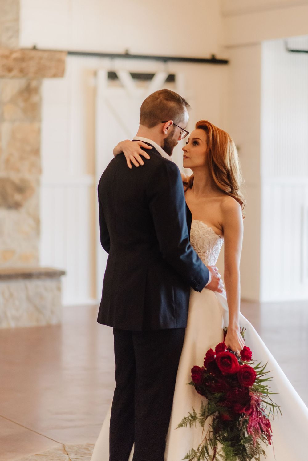 A romantic wedding moment with a couple embracing in formal attire near a stone wall.