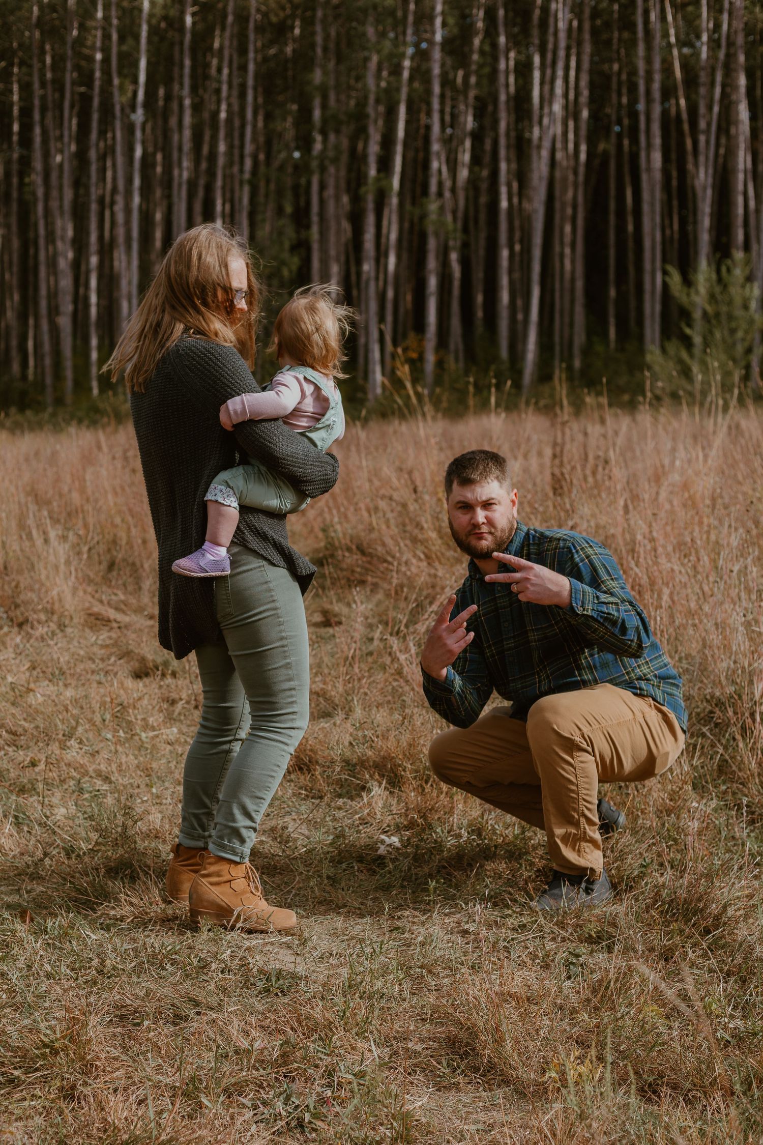 A family enjoying a tender moment together in a serene forest setting with tall trees and golden grass.