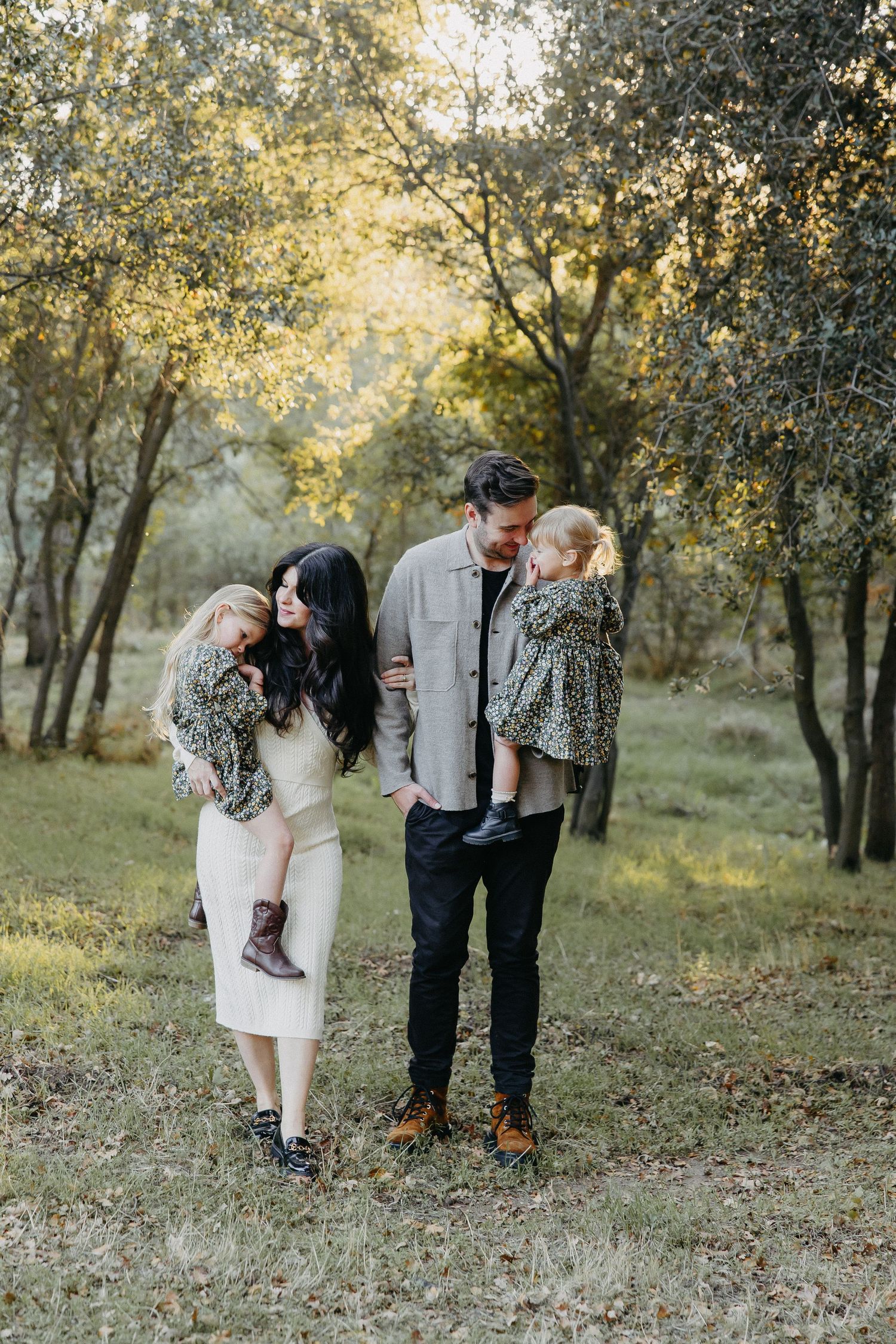 A family shares a tender outdoor moment together in a sunlit woodland setting during golden hour.
