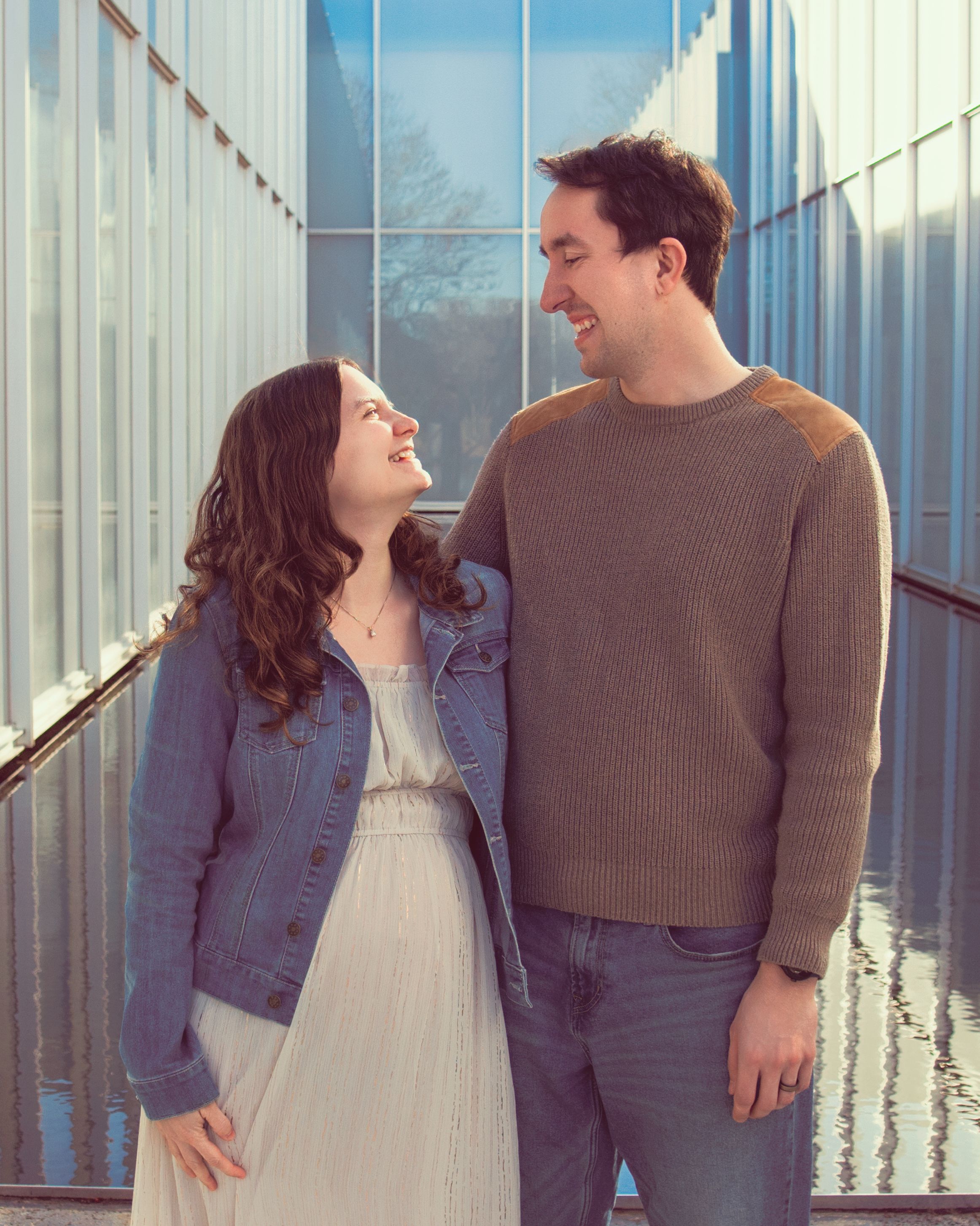 A couple shares a happy moment together in a sunlit corridor with glass walls.