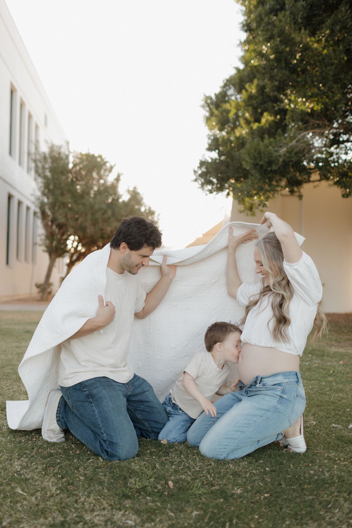 A playful family moment under a white blanket on green grass outdoors.