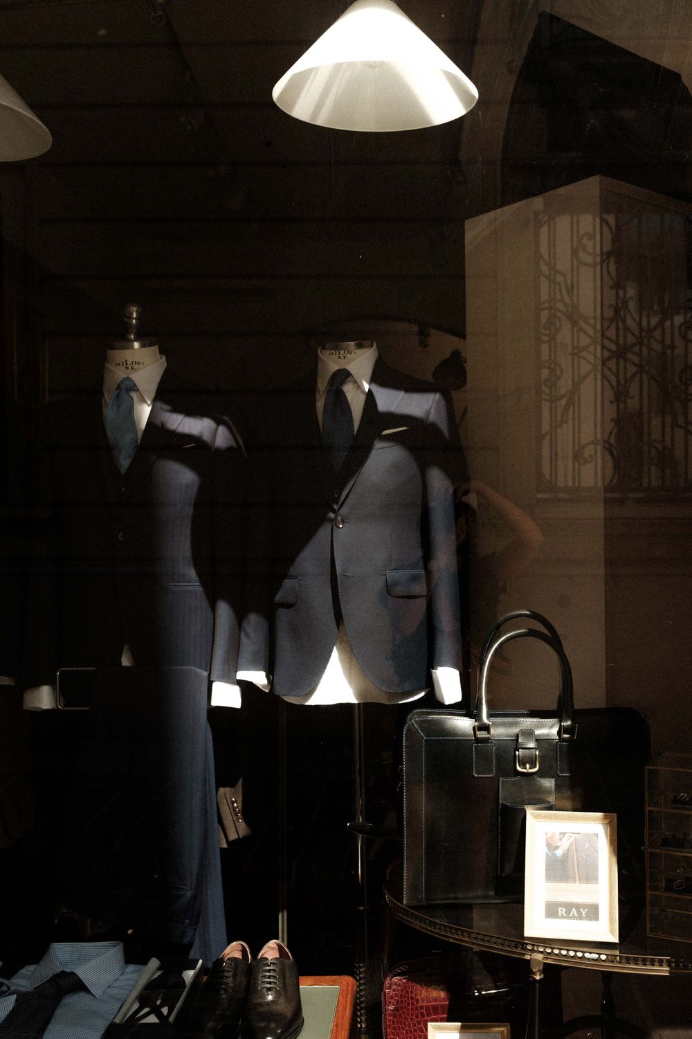 Display window of a menswear shop showing formal suits and accessories under dramatic lighting.