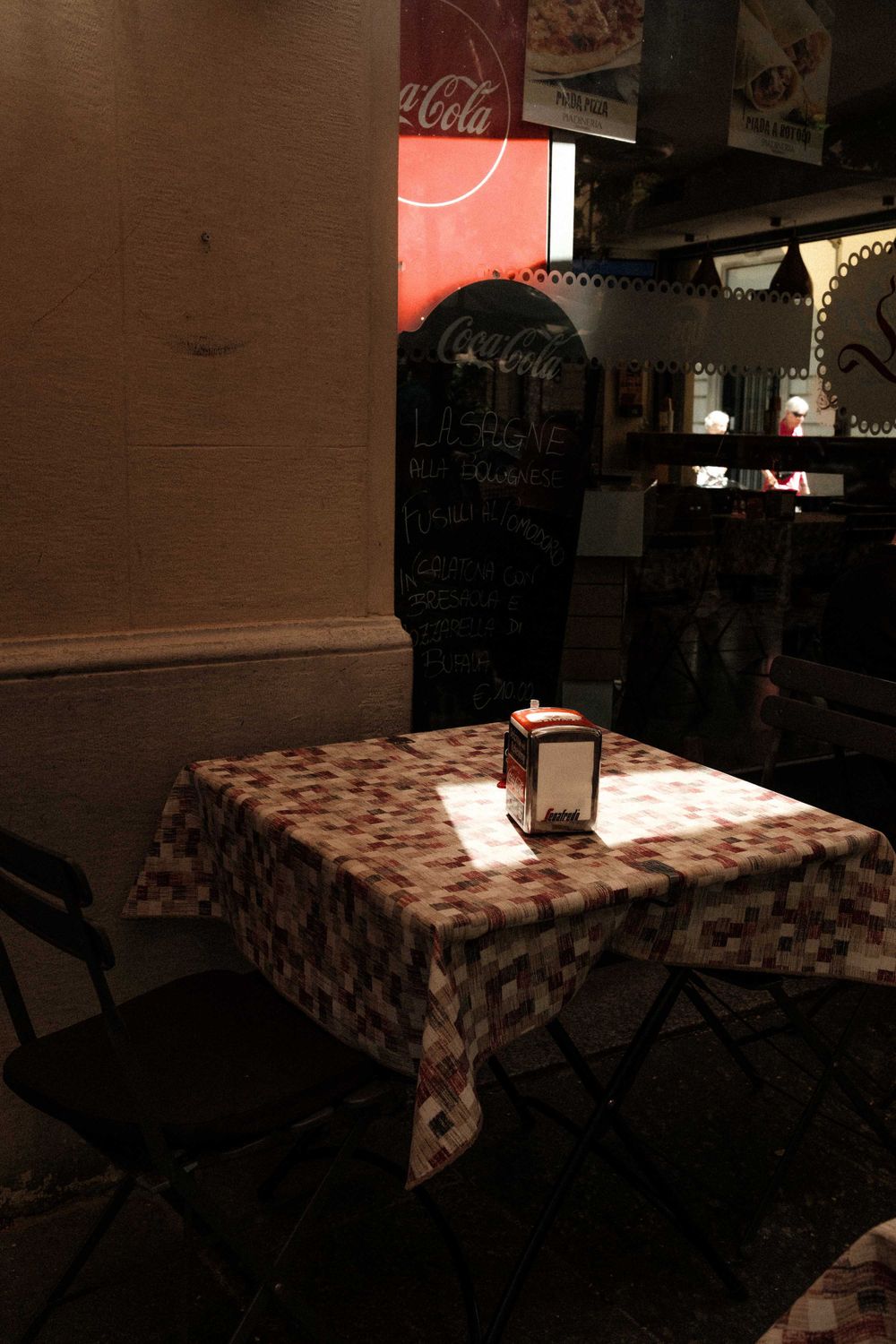 A cozy restaurant table with patterned tablecloth illuminated by a single beam of light.