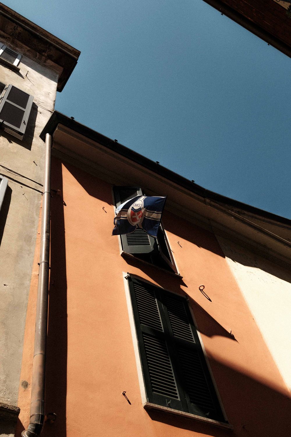 Low angle view of a peach colored building facade with black shutters and blue sky in Italy.