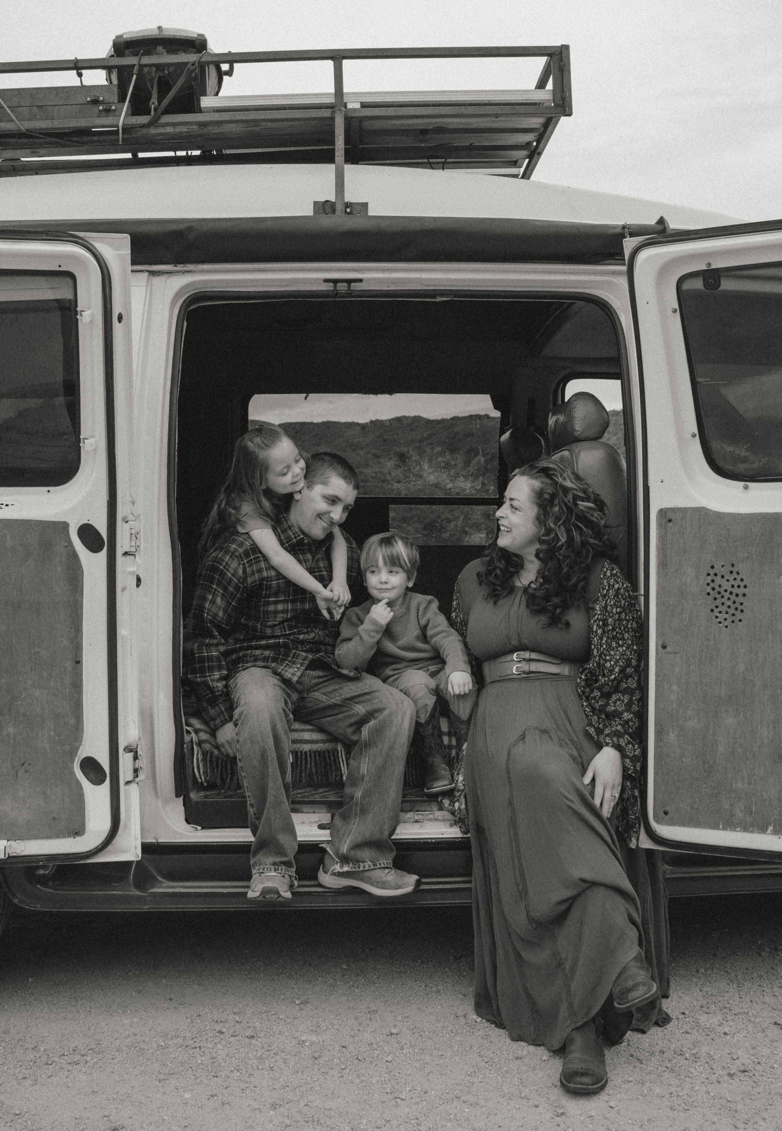 A black and white photograph showing a candid moment inside a van with people chatting in a casual setting.