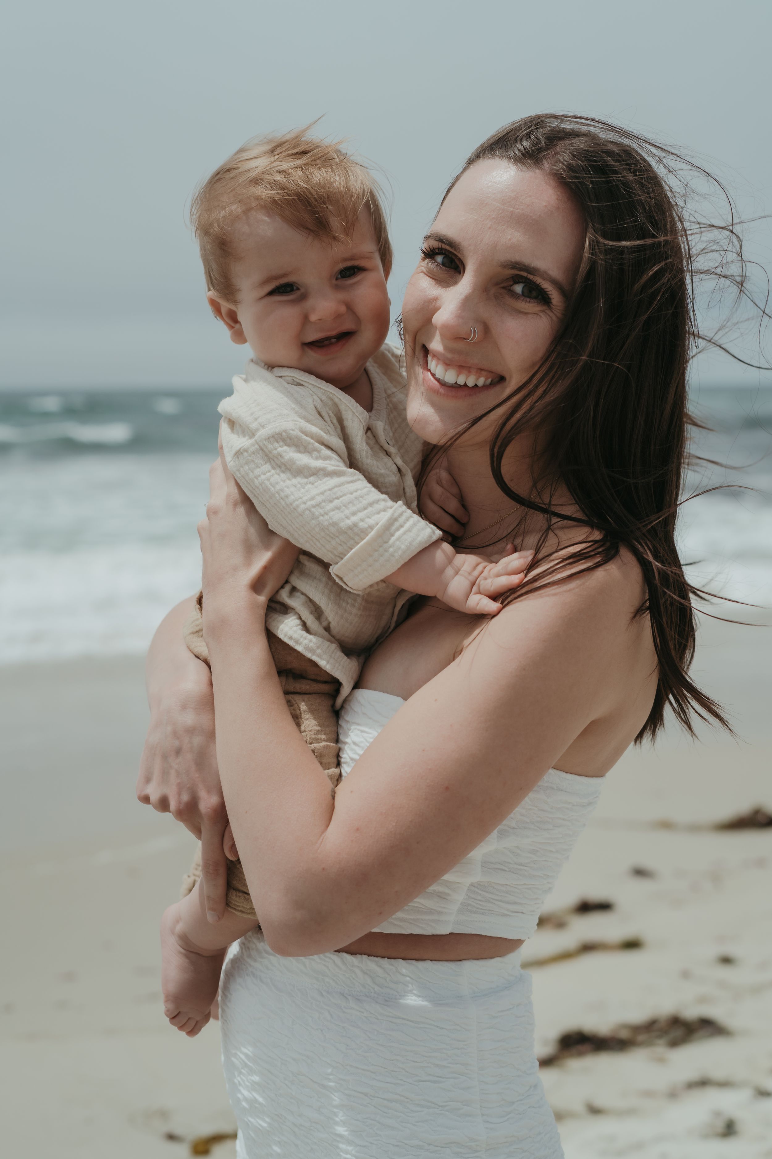 Parent and child share joyful moments together while playing on a sunny beach with waves in the background.