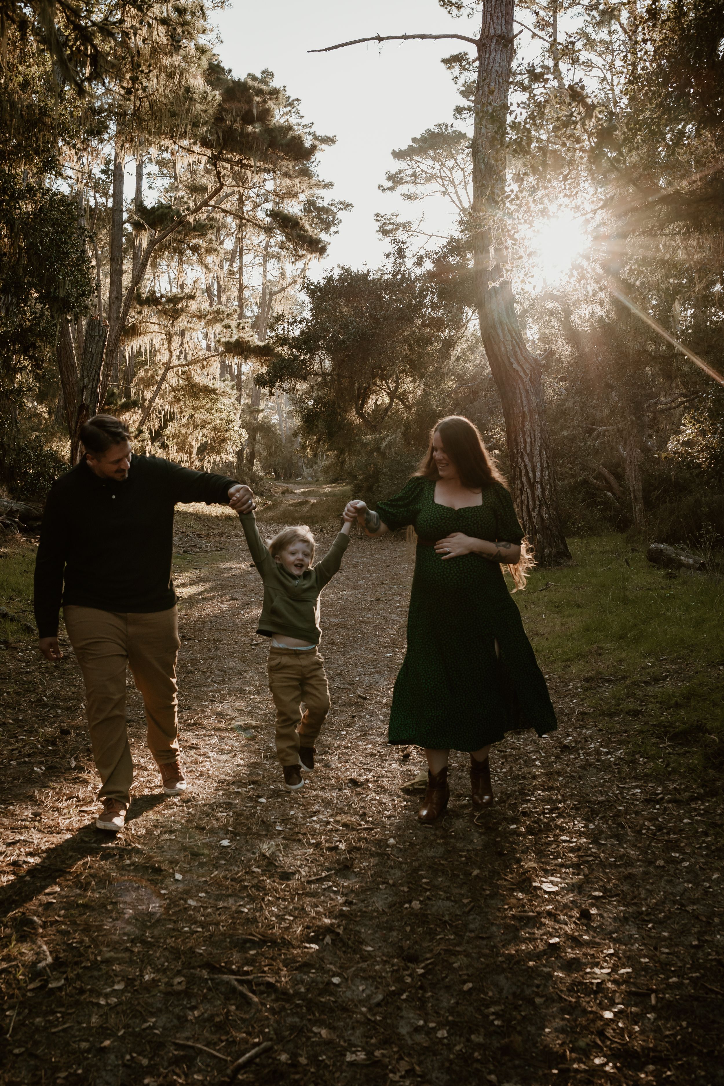 A family enjoys a joyful moment together on a forest path with sunlight streaming through the trees in a golden sunset.