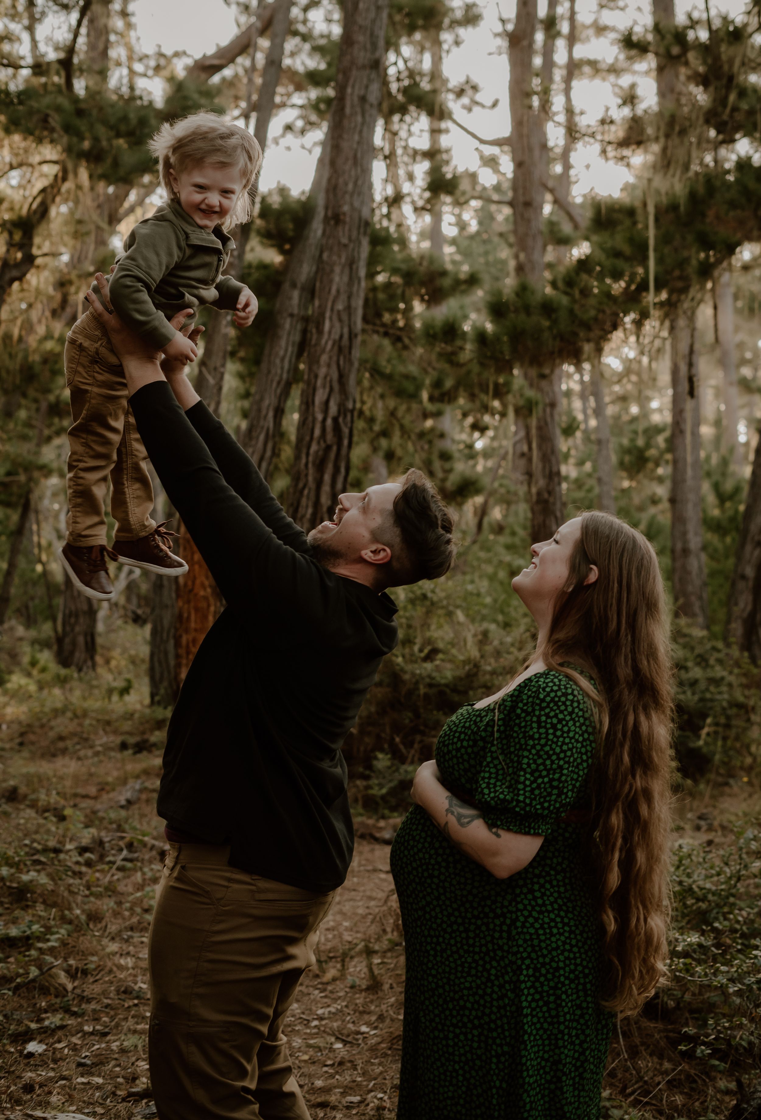 A loving outdoor family moment captured in a forest setting with earthy autumn tones in their coordinated outfits.