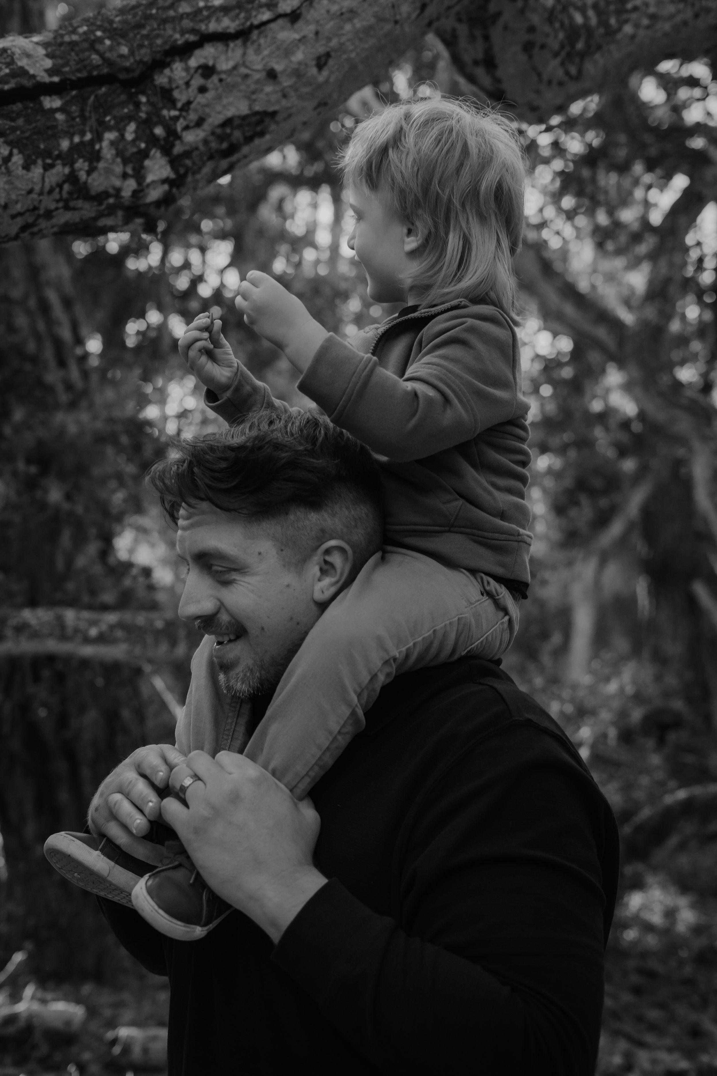 A heartwarming black and white photo showing a playful shoulder ride moment between parent and child in nature.