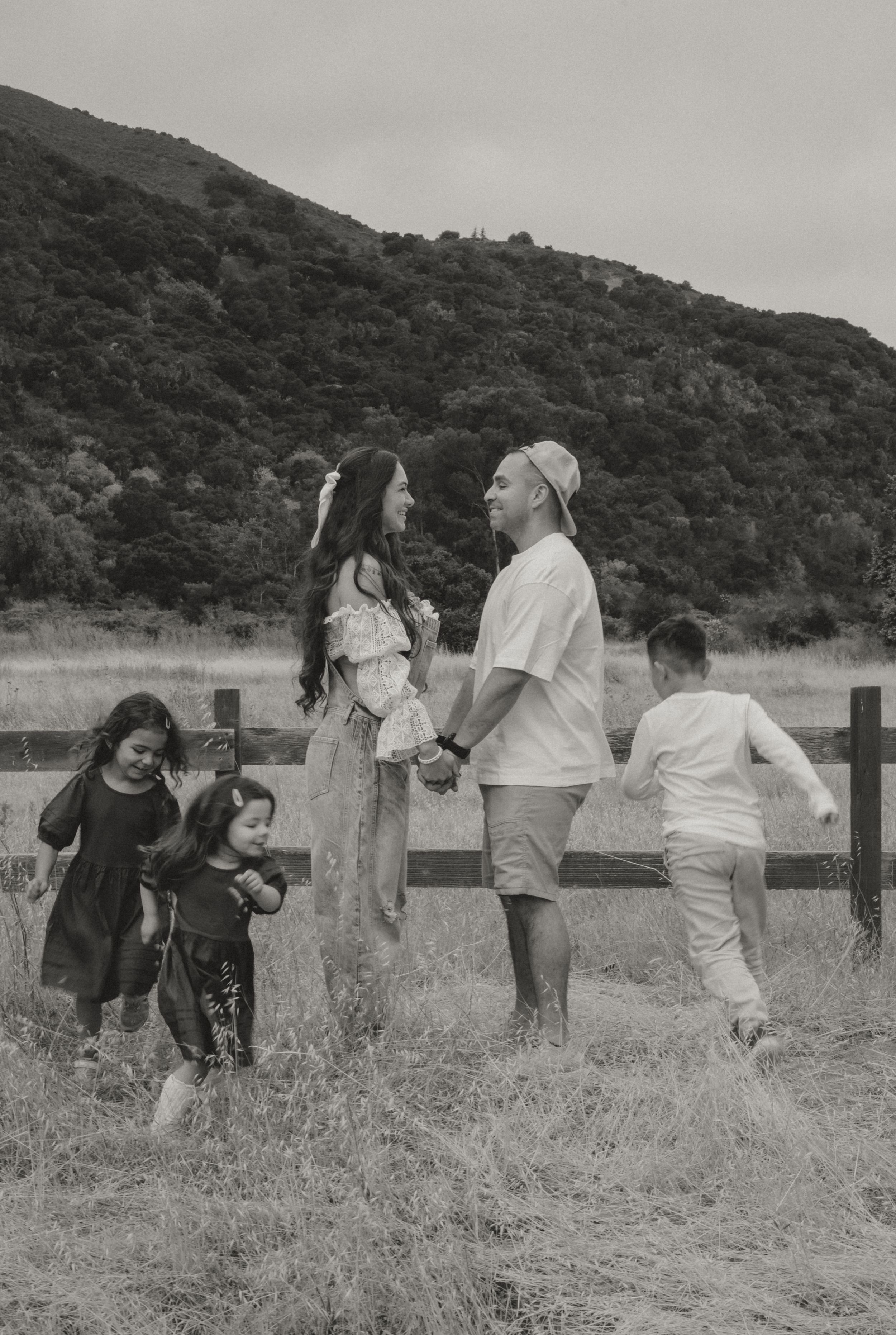 A group of people enjoying time together outdoors near a wooden fence with rolling hills in the background.